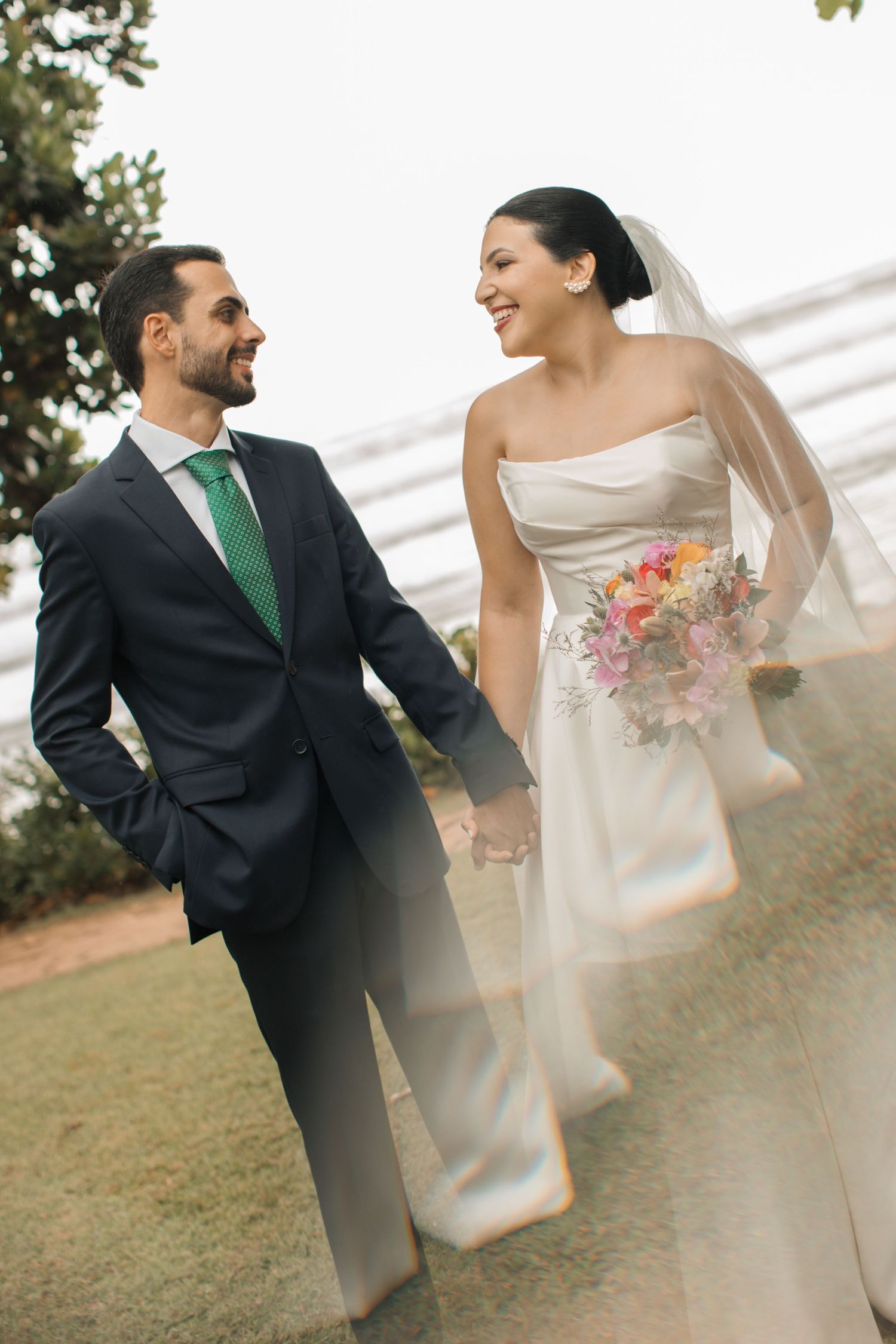 Couple in wedding attire sharing a playful moment on grassy hillside.