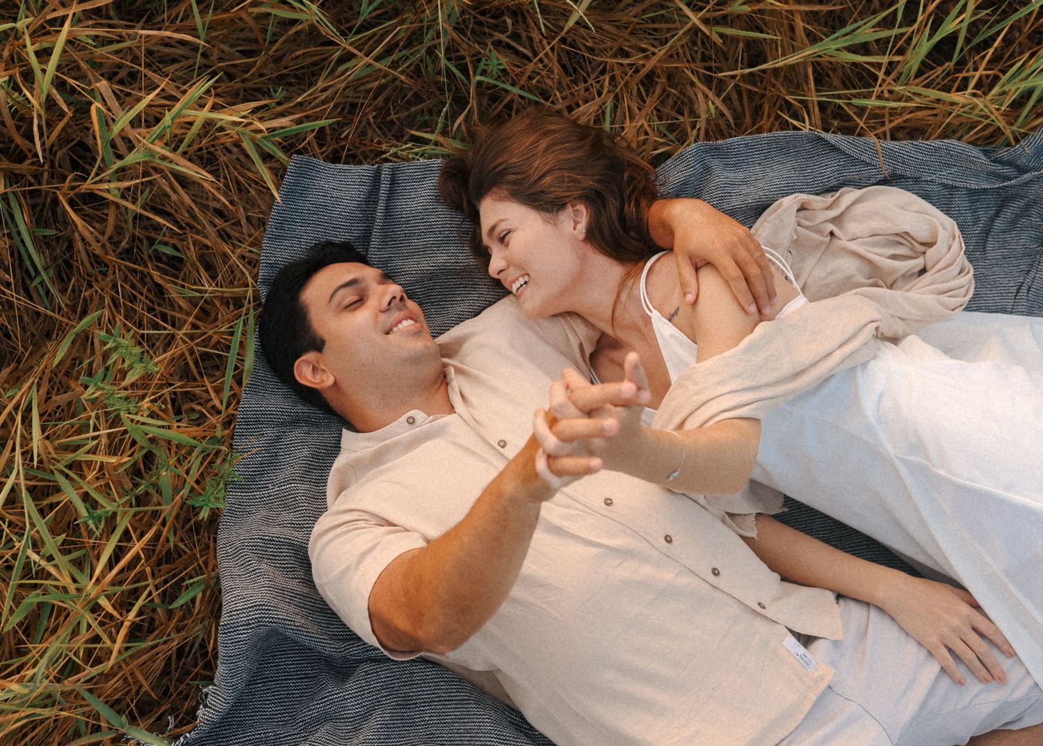 A couple lying together on a blanket in tall grass during a sunset photoshoot.