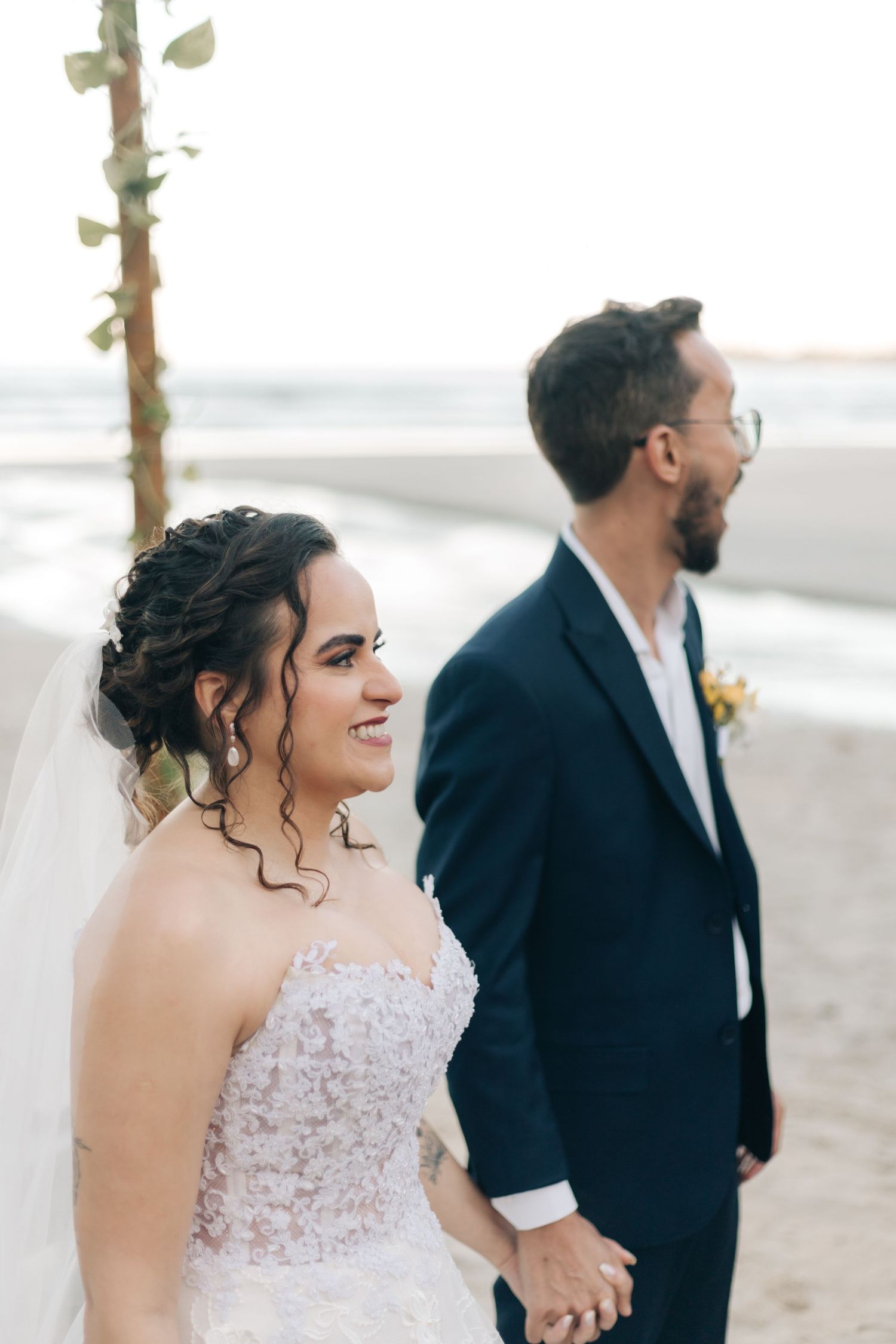 A wedding couple poses on a beach at sunset in formal attire.
