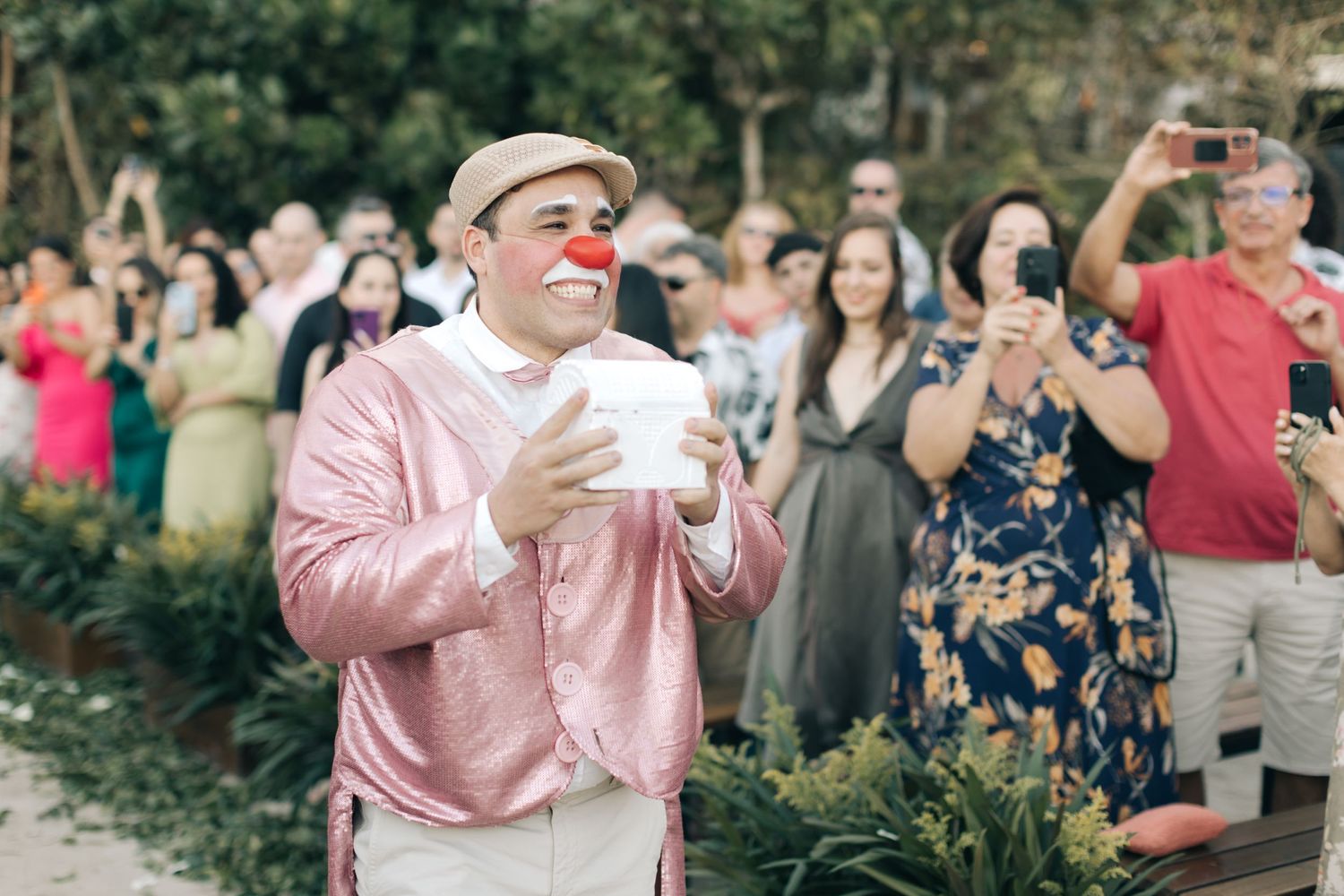 Performer in pink jacket and clown nose entertains crowd at outdoor gathering.