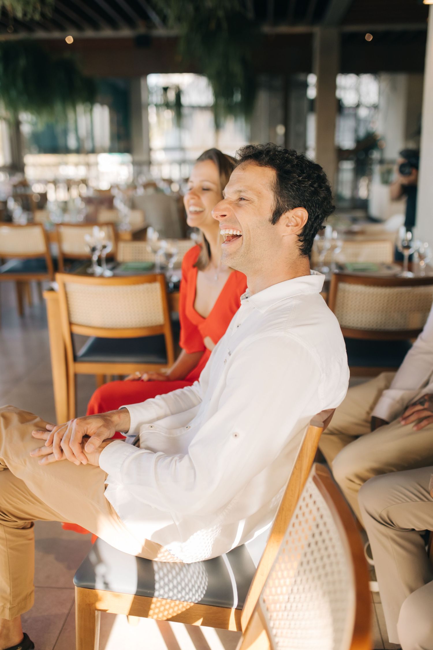 Wedding guests laughing together while seated at a reception with warm lighting.