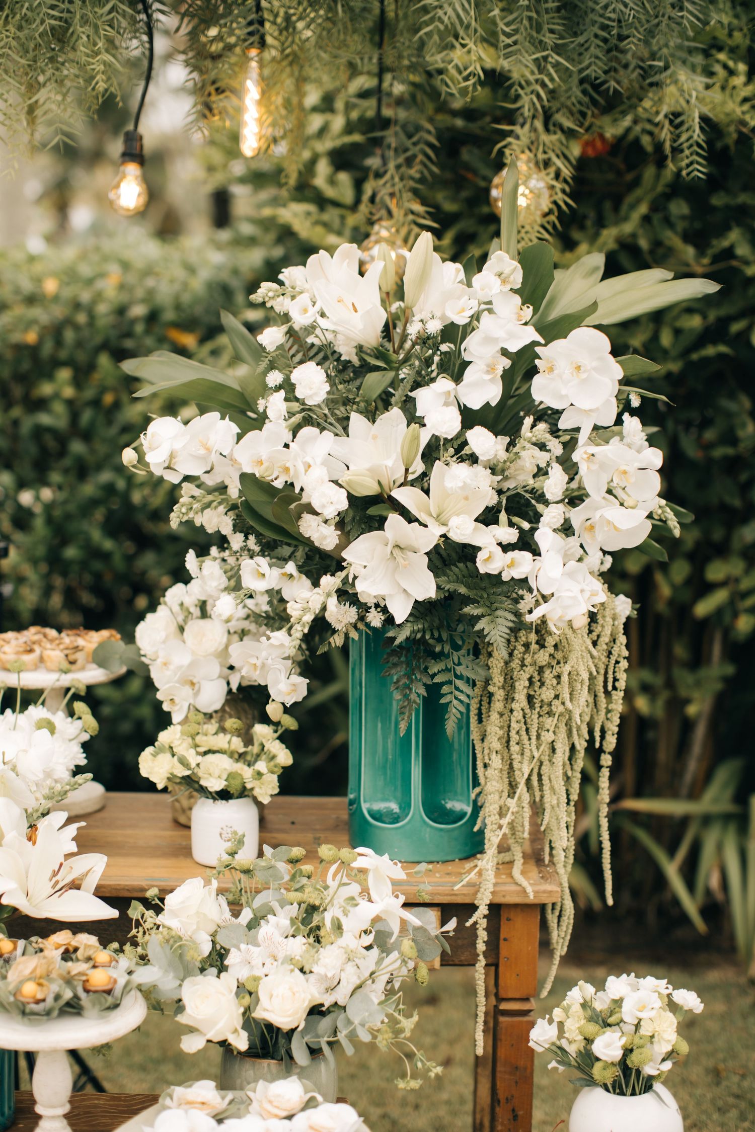 Stunning white flower arrangement in a turquoise vase with hanging string lights above.
