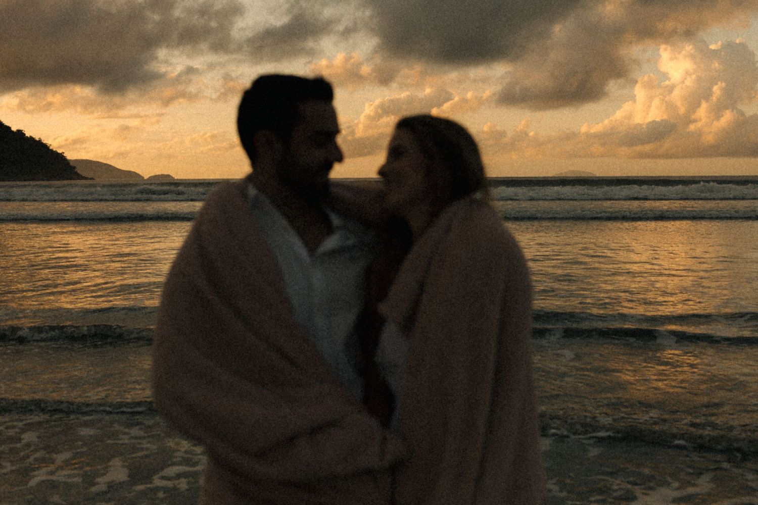 Silhouetted figures share an intimate moment by the ocean during a dramatic sunset.