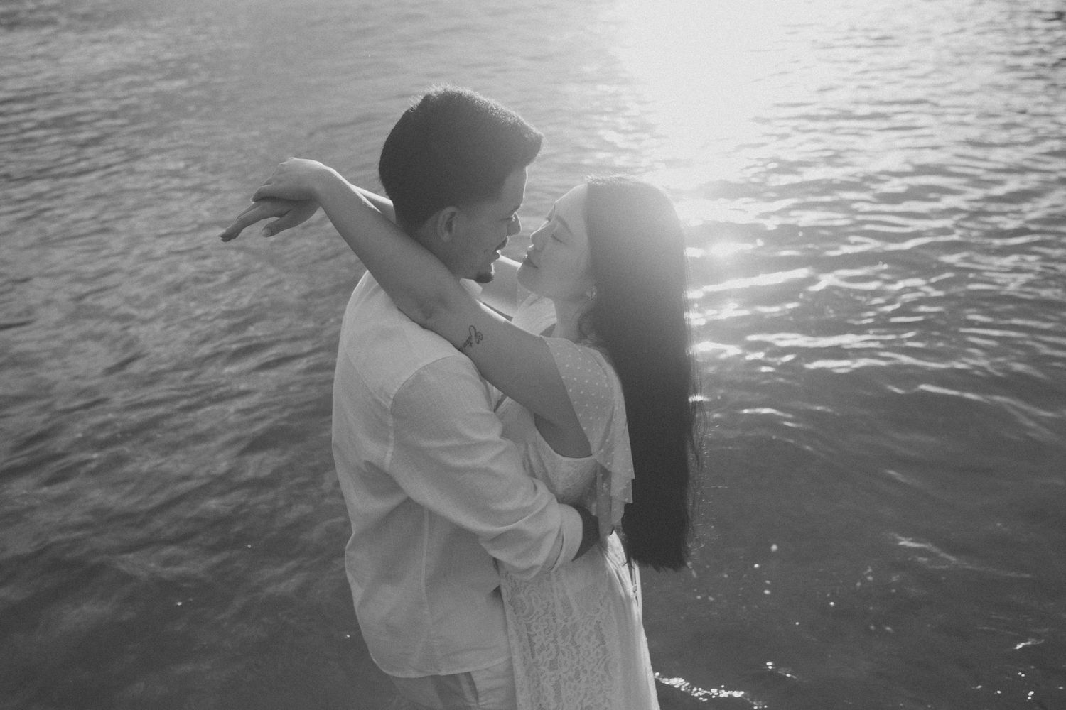 A romantic black and white moment captured against sparkling water at sunset.