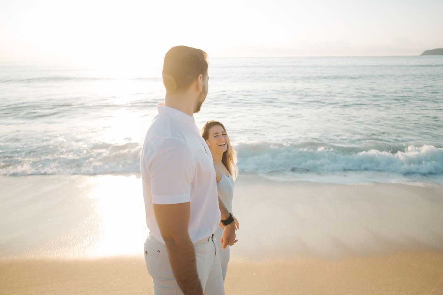 Couple sharing intimate moment on beach during sunset with waves crashing behind them.