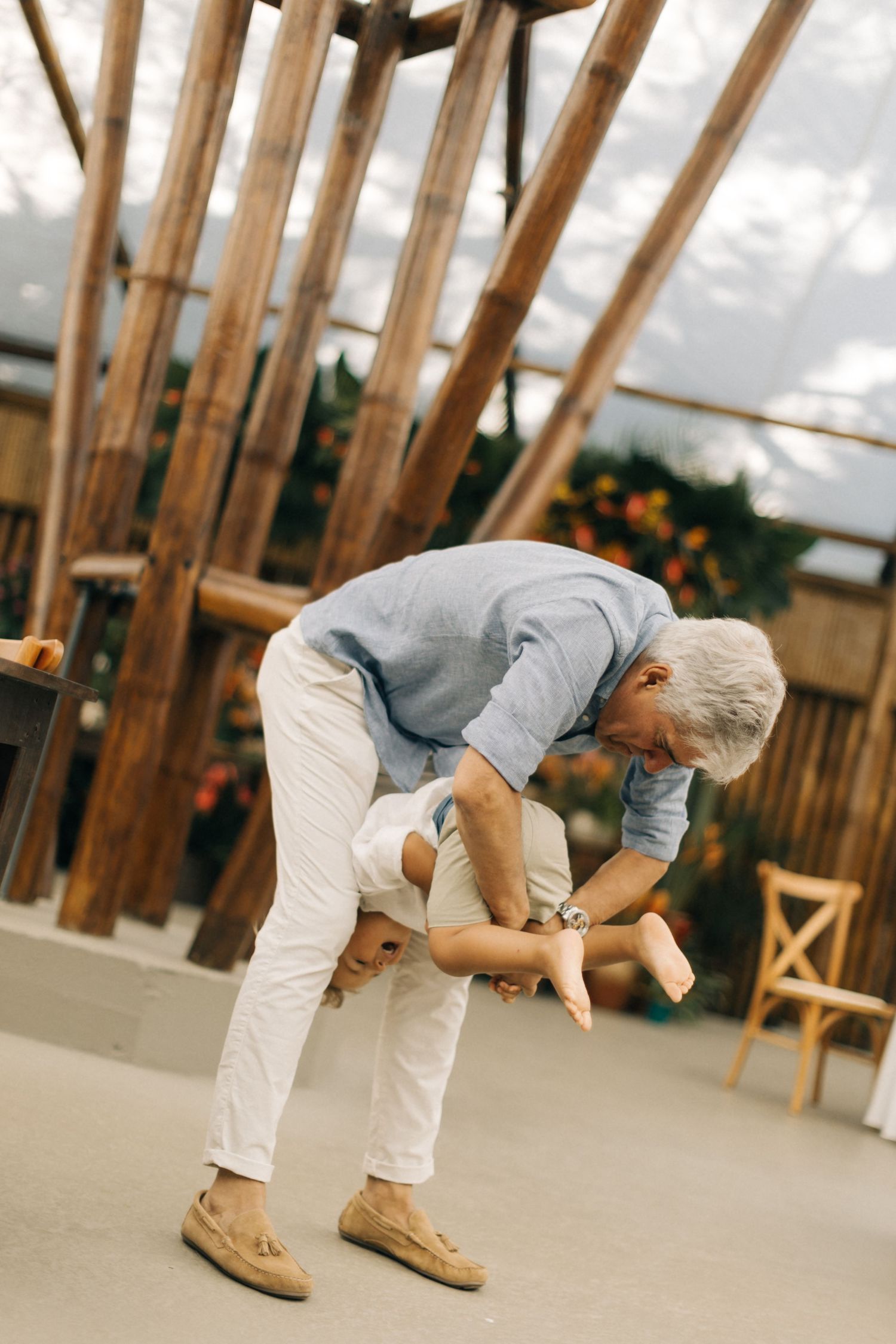 Someone in a gray shirt and white pants bends forward in a wooden-framed space.