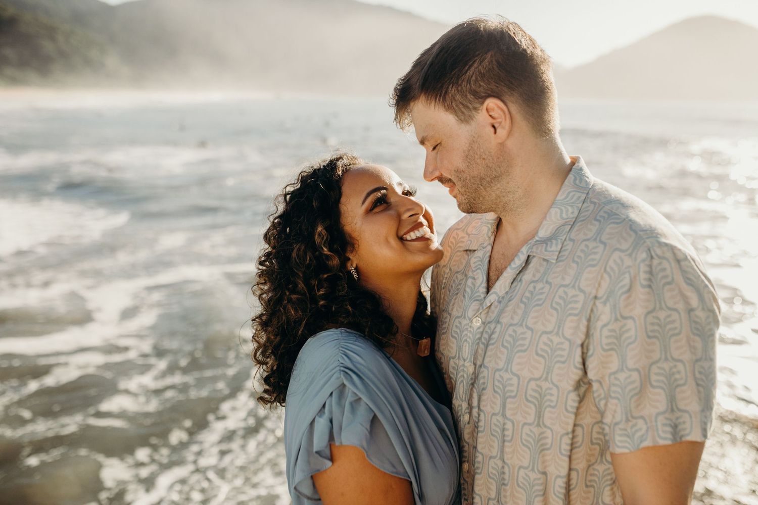Joyful moment shared between couple against dramatic coastal backdrop at sunset.