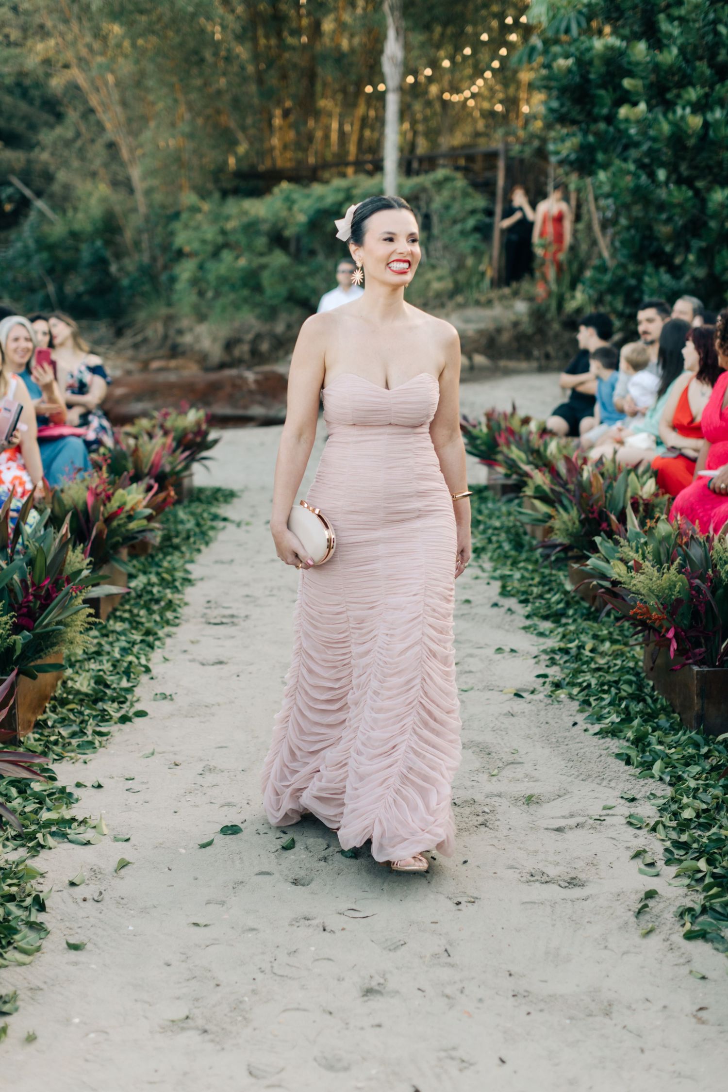 Bridesmaid in blush pink ruched gown walks down garden pathway at outdoor wedding.