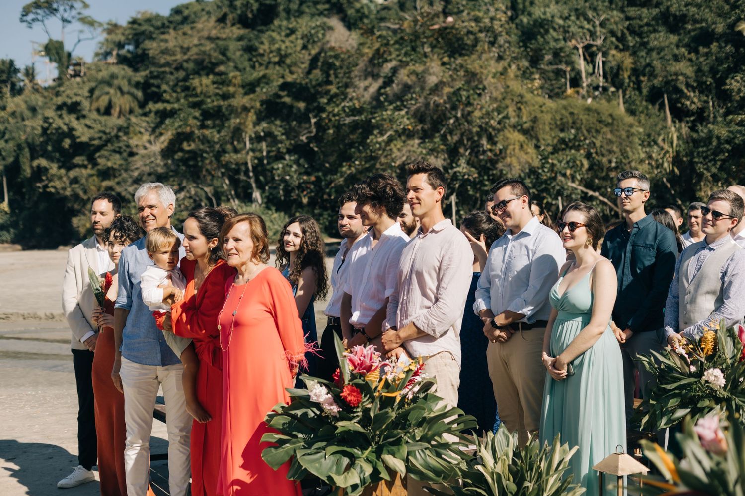 Wedding guests gathered outdoors wearing colorful attire for group photos.