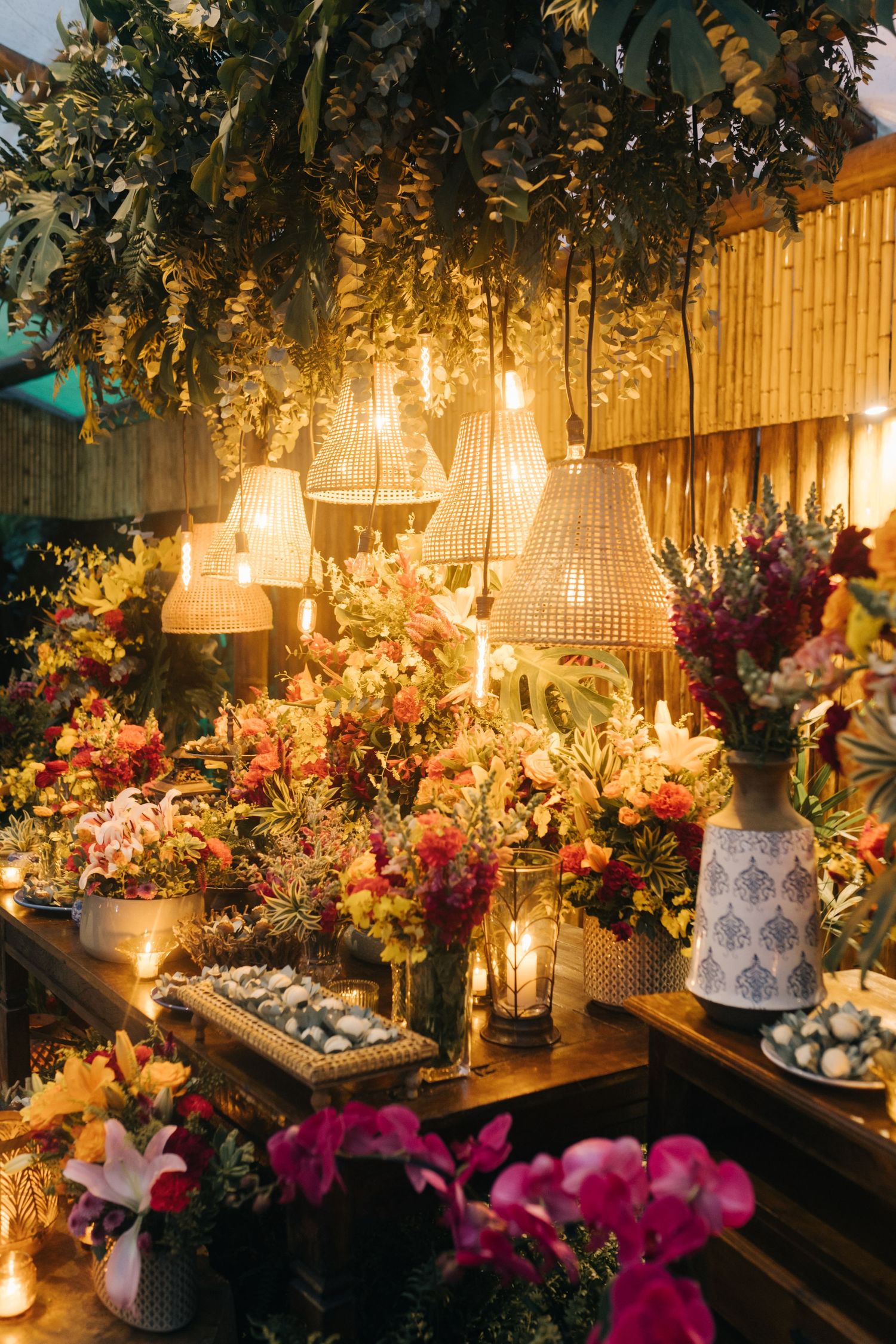 Luxurious wedding dessert table with hanging wicker lamps and vibrant floral arrangements.