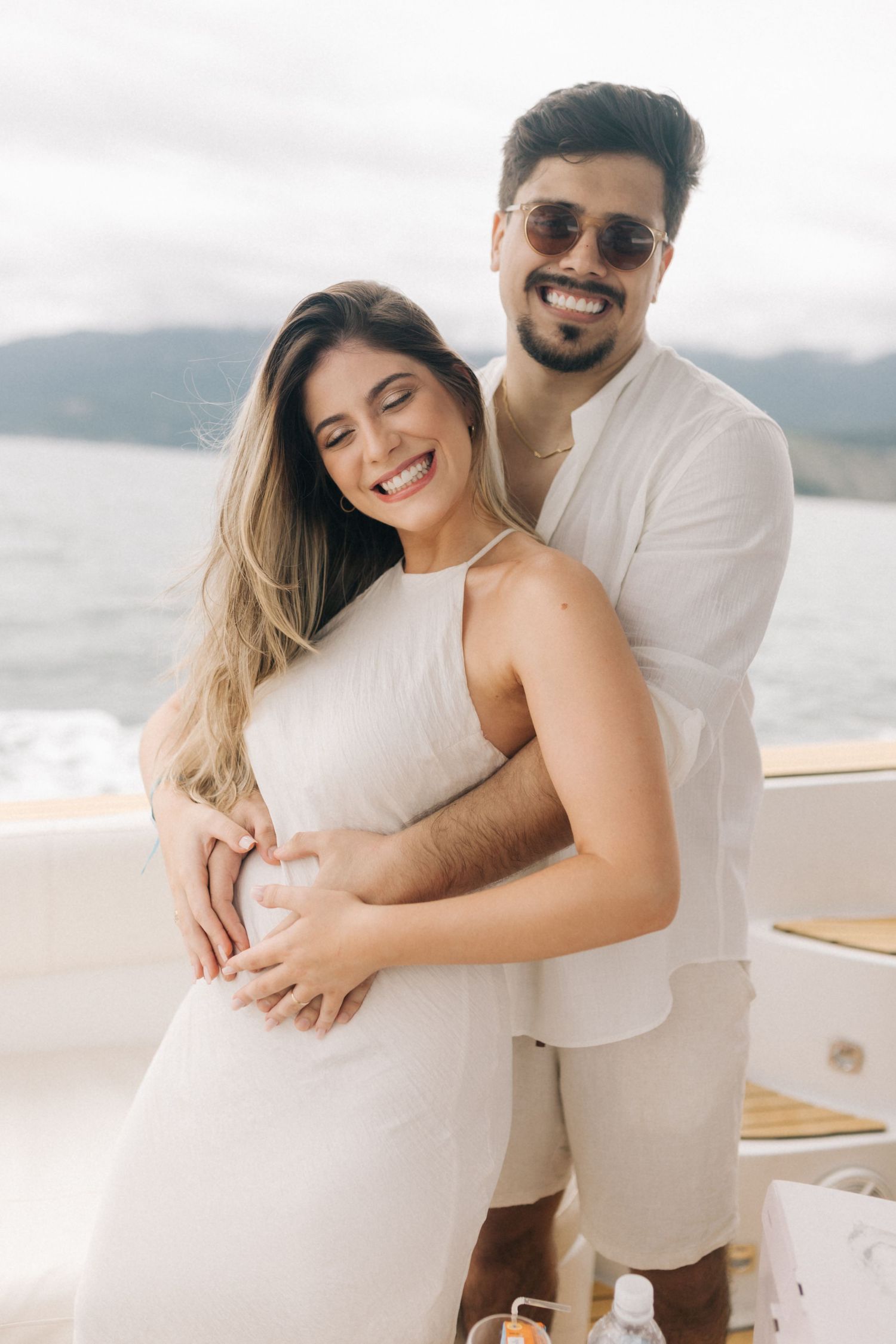 Loving couple in white outfits sharing a joyful moment on a boat deck.