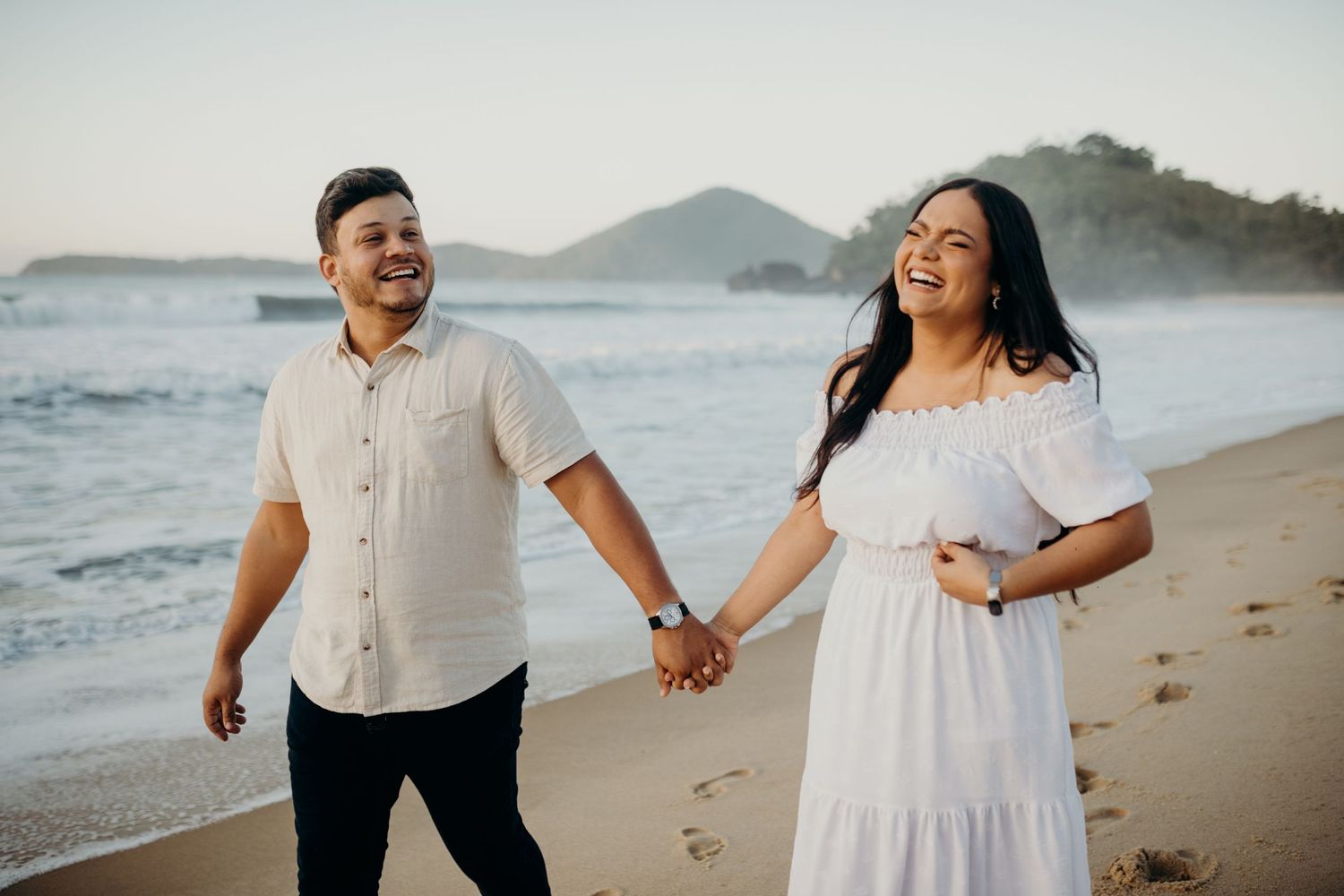 Couple shares romantic moments on a beach at sunset with mountains in the background.