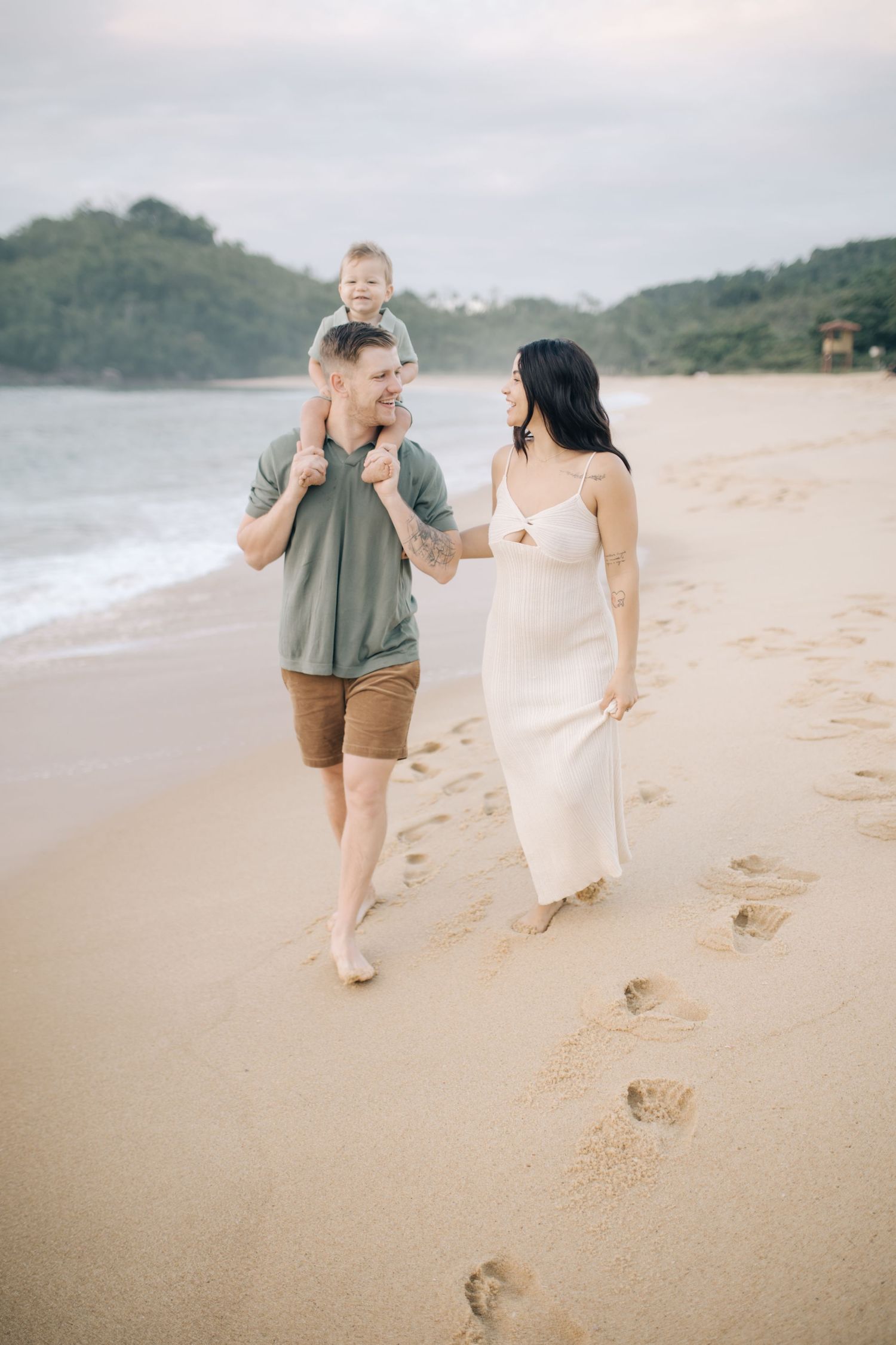 A family takes a stroll along a scenic beach with mountains and ocean views.