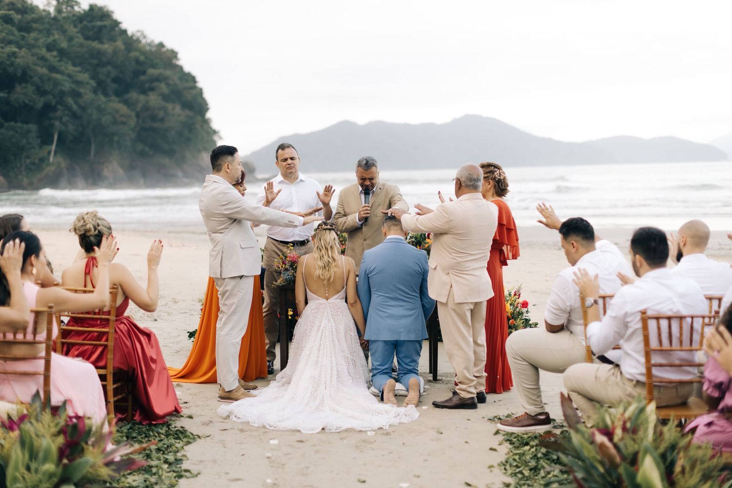 Wedding party arranged on a scenic beach with mountains and ocean in the background.
