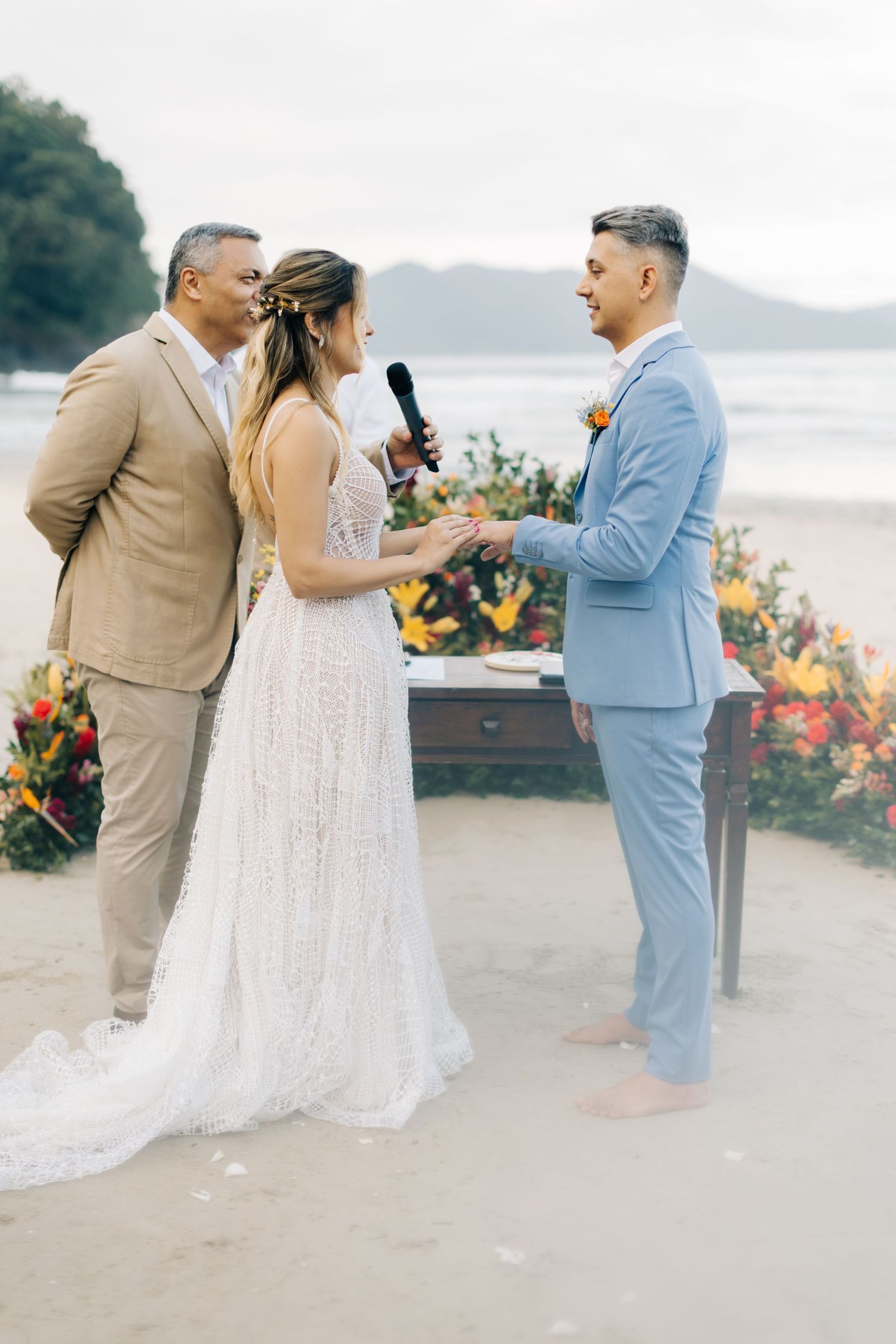 Wedding ceremony on a beach with vibrant floral arrangements and officiant speaking into microphone.