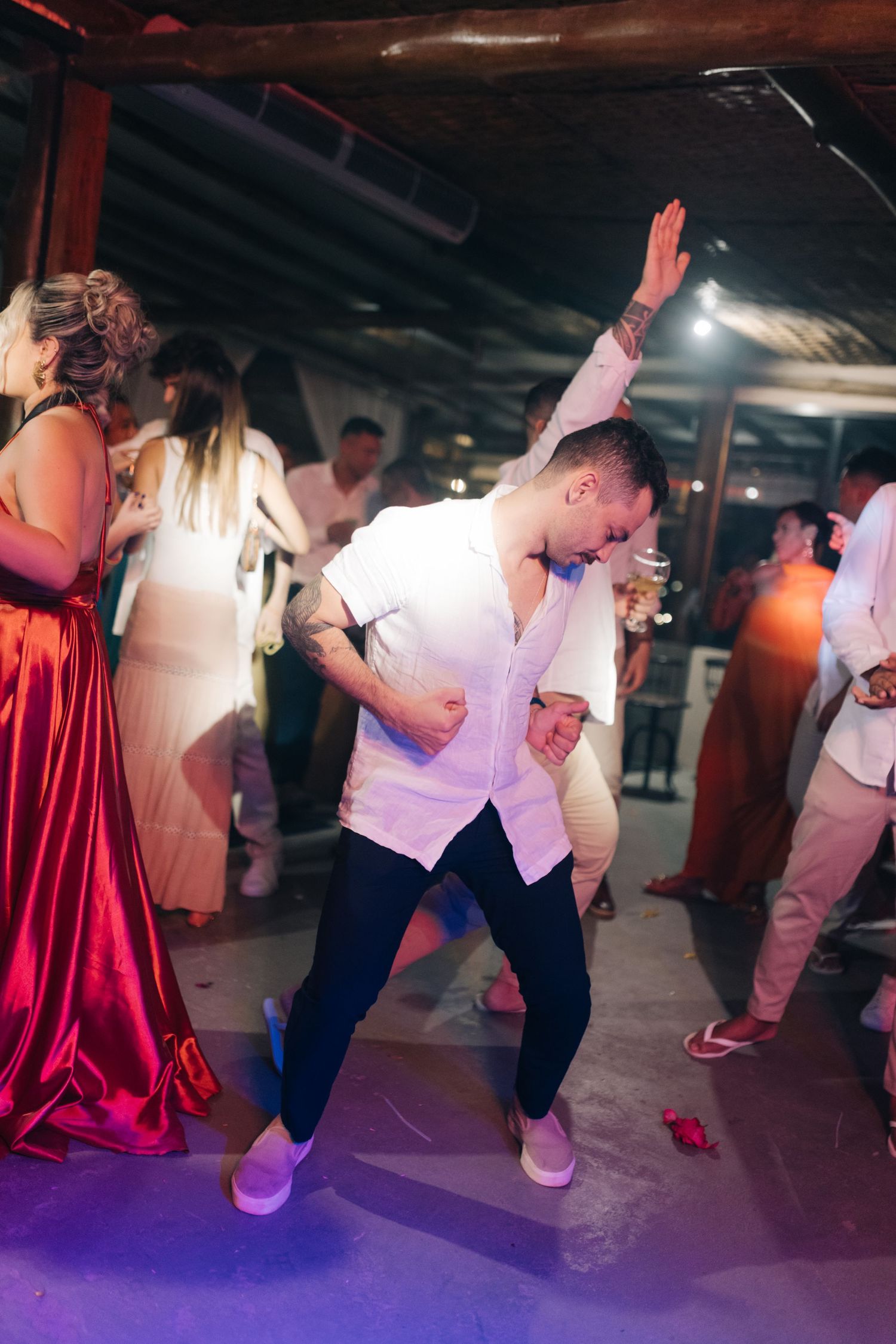 Guest dancing under purple lighting at wedding reception with red dress visible in background.