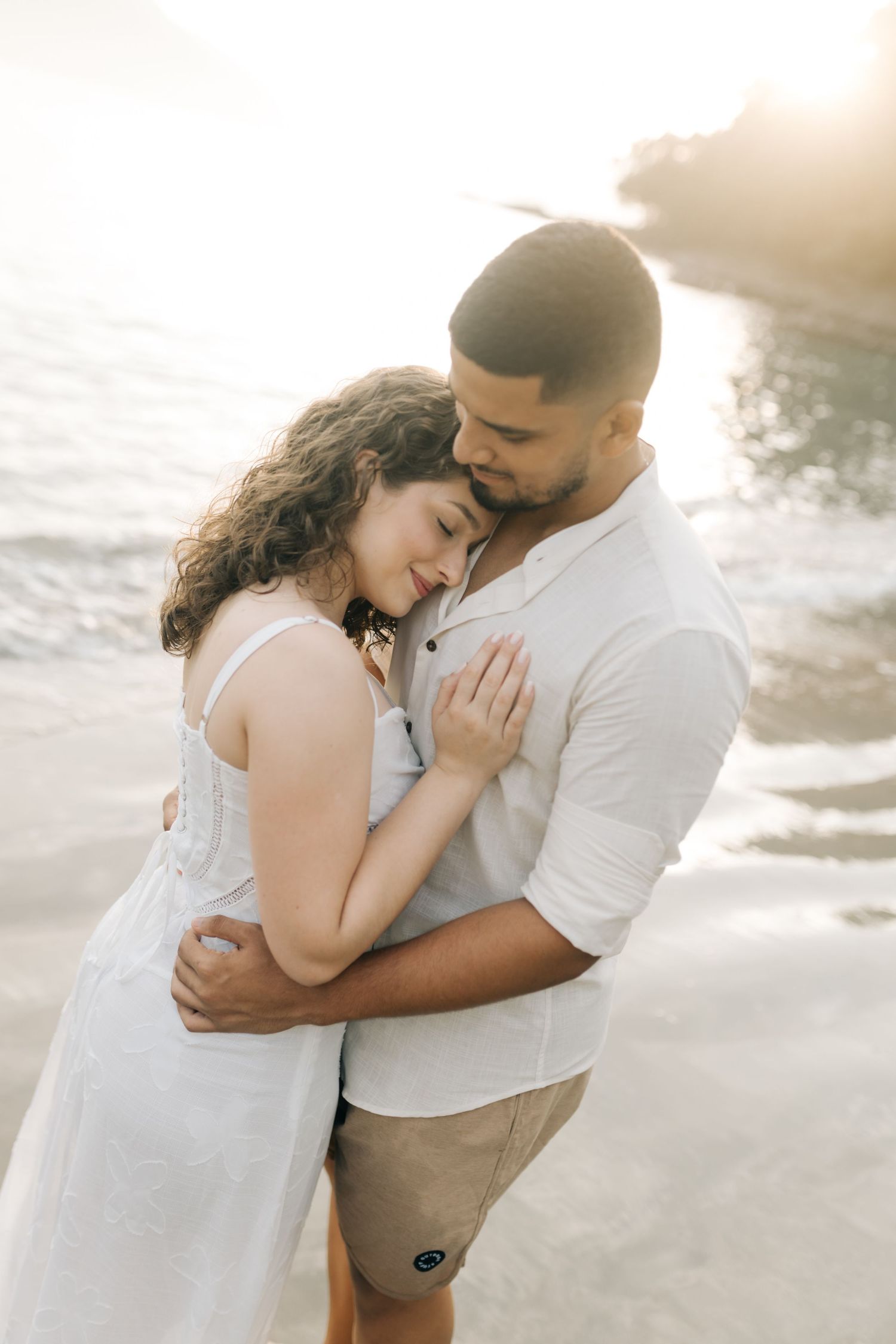 Intimate embrace of a couple in white outfits on a sunset beach.