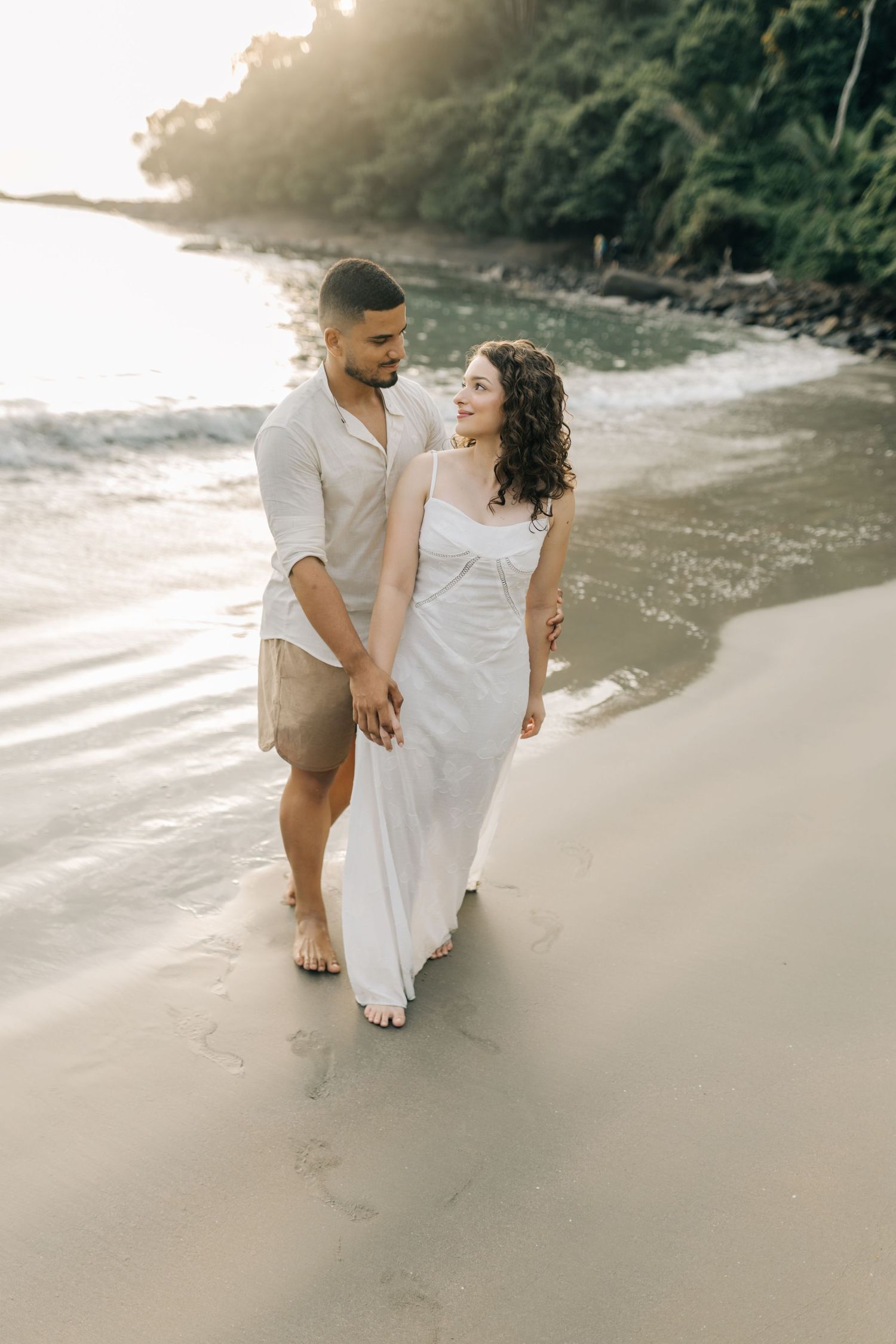 Side view of couple walking along beach shoreline during sunset photo session.