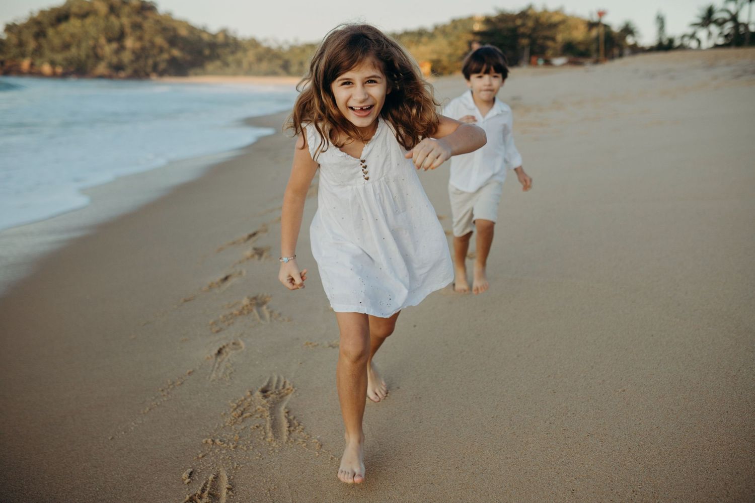 Children running and playing on a scenic beach with mountains in background.