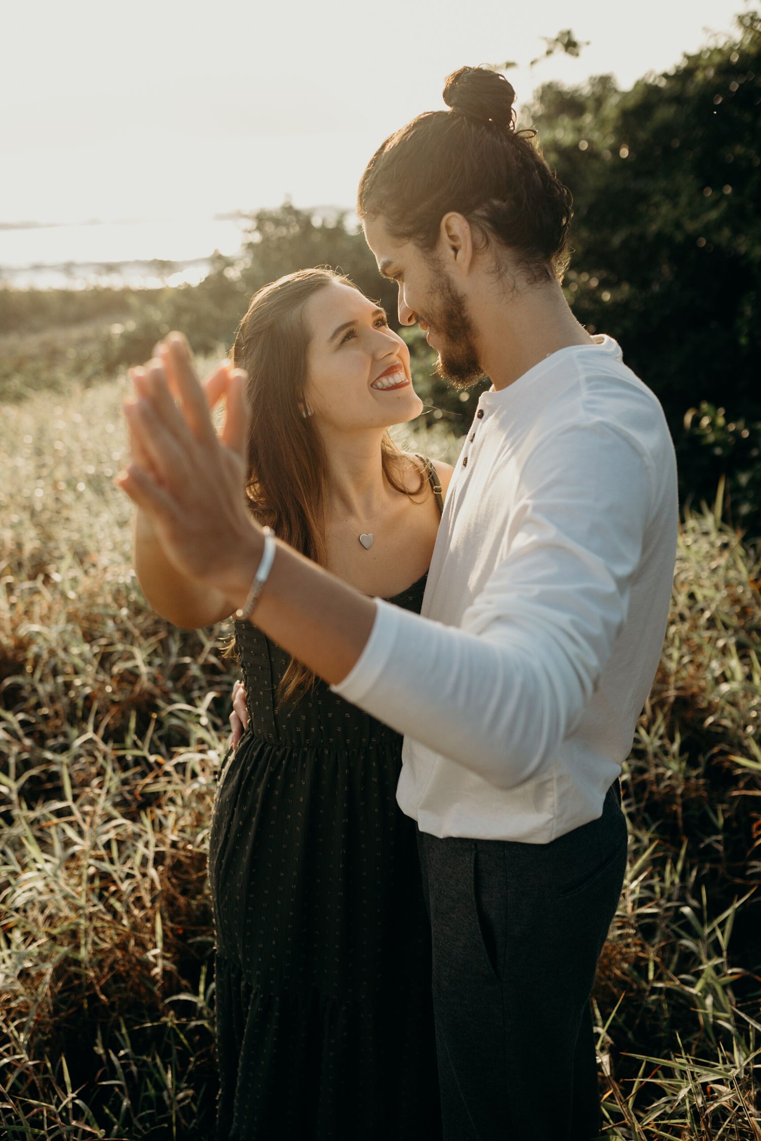 Happy couple dances together in field during sunset photoshoot.