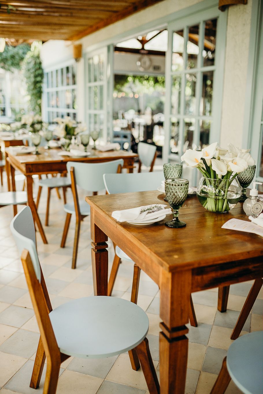 Elegant outdoor dining setup with wooden tables, blue chairs, and white floral centerpieces.