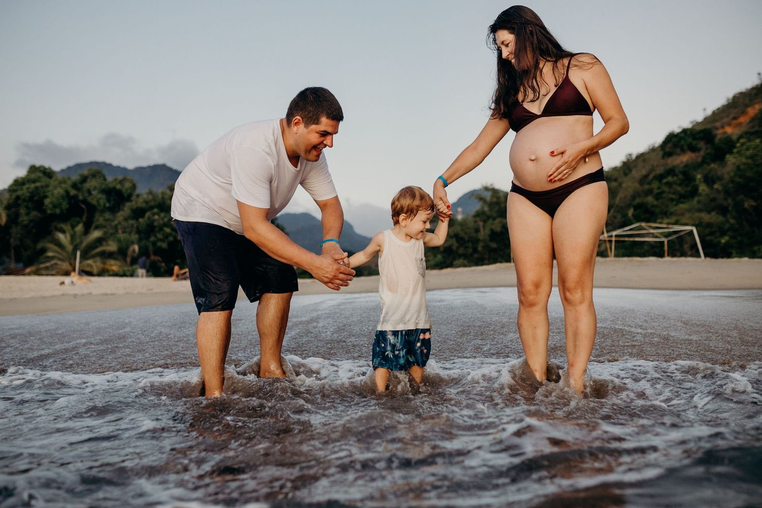 Family members bent down exploring the shallow waters at the beach shore.