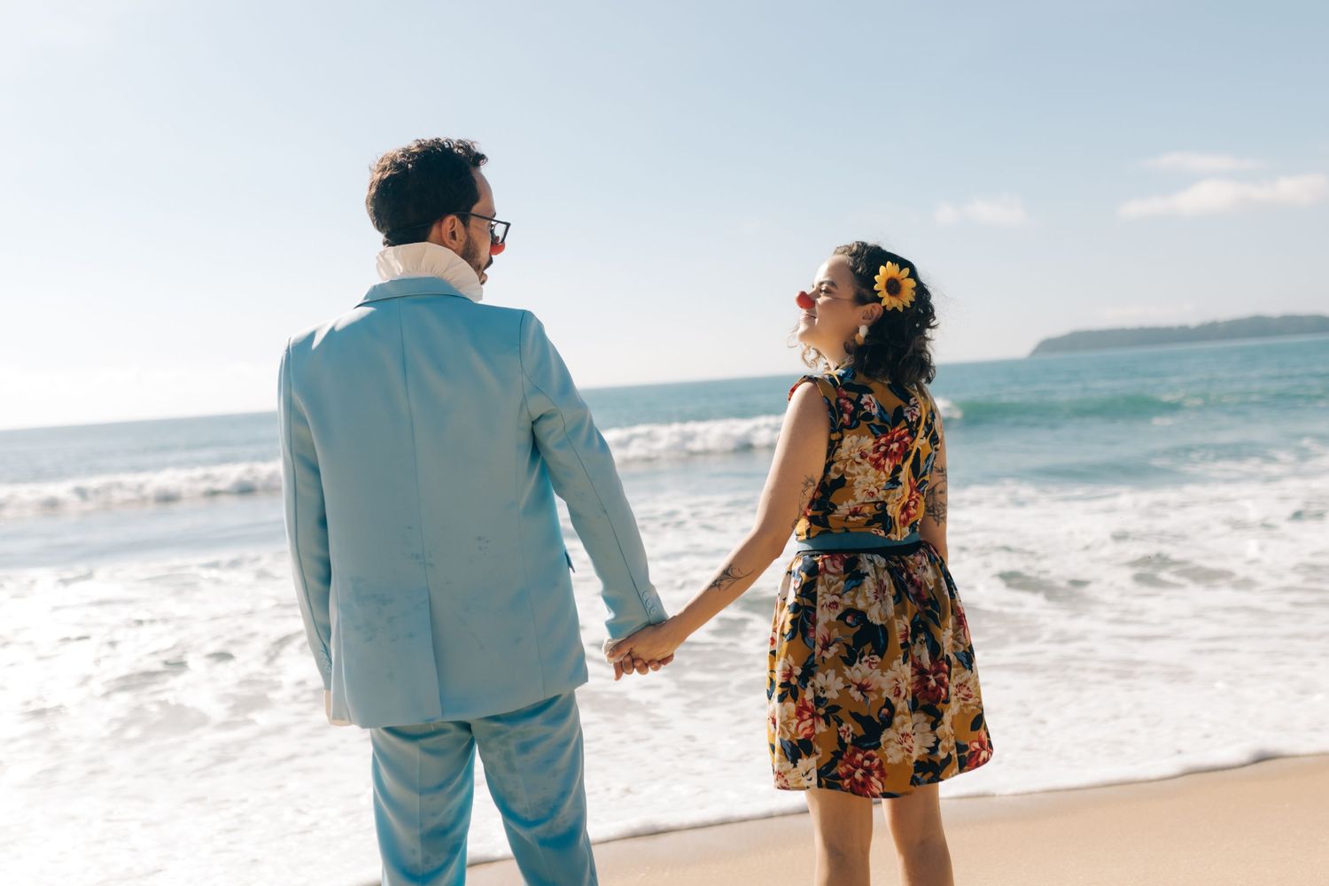 A couple holds hands while enjoying the ocean view on a sunny beach day.