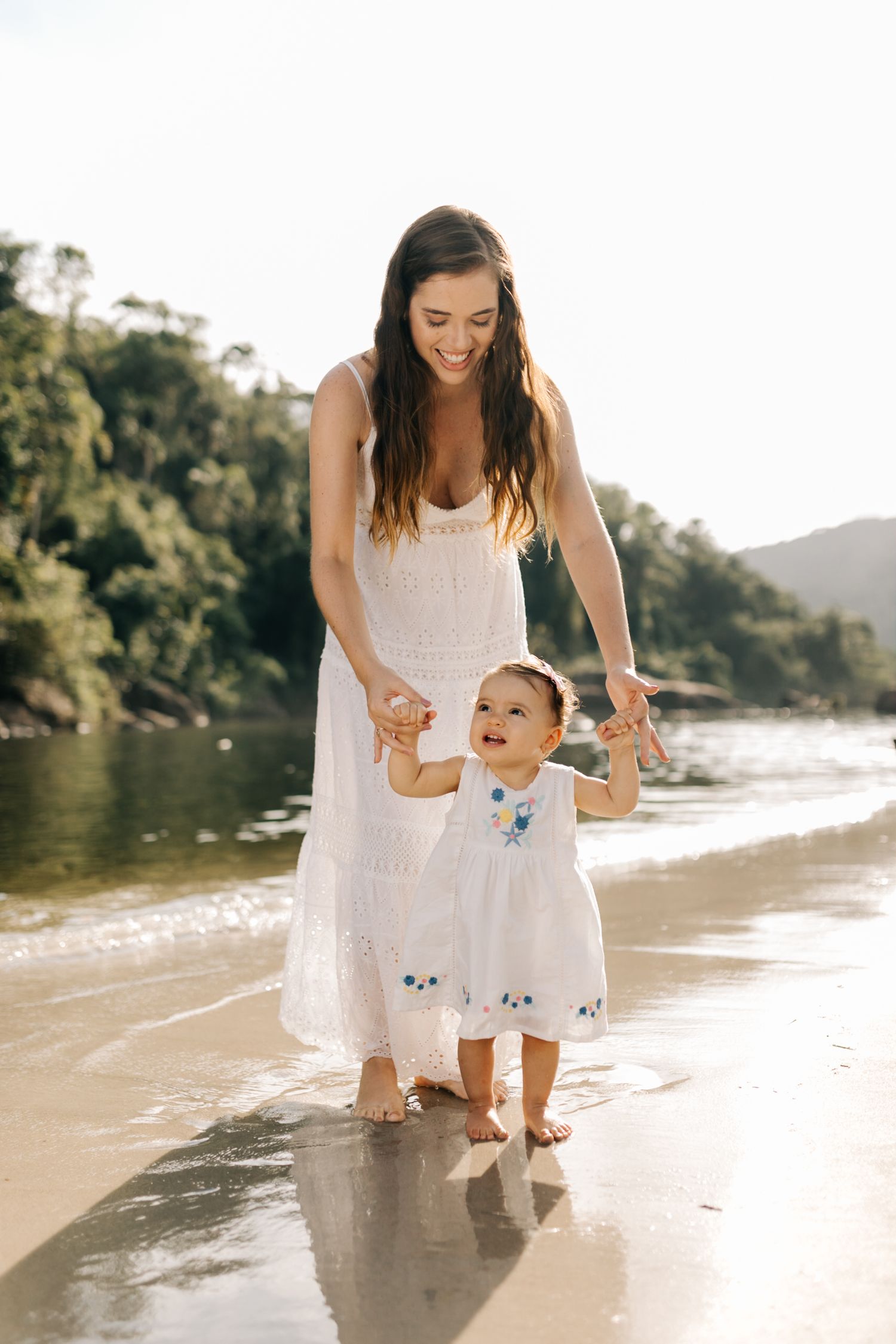 A beautiful beach photoshoot shows a family walking along the shoreline in white outfits.