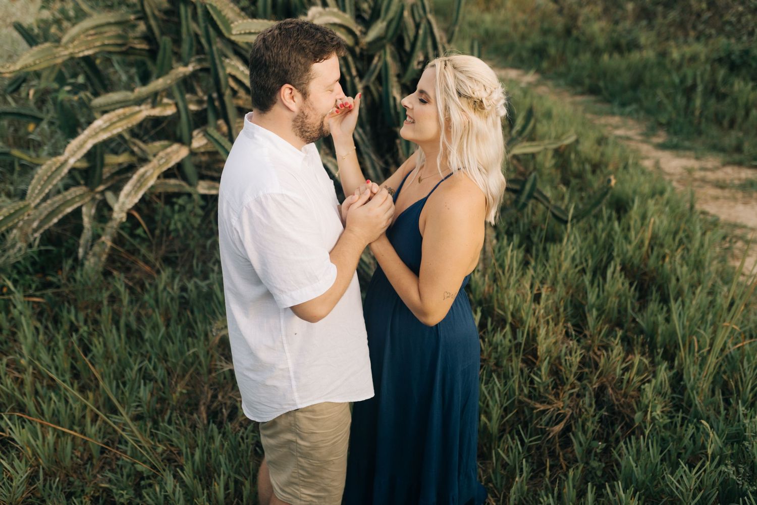 Intimate moment between couple surrounded by coastal vegetation and mountain landscape.