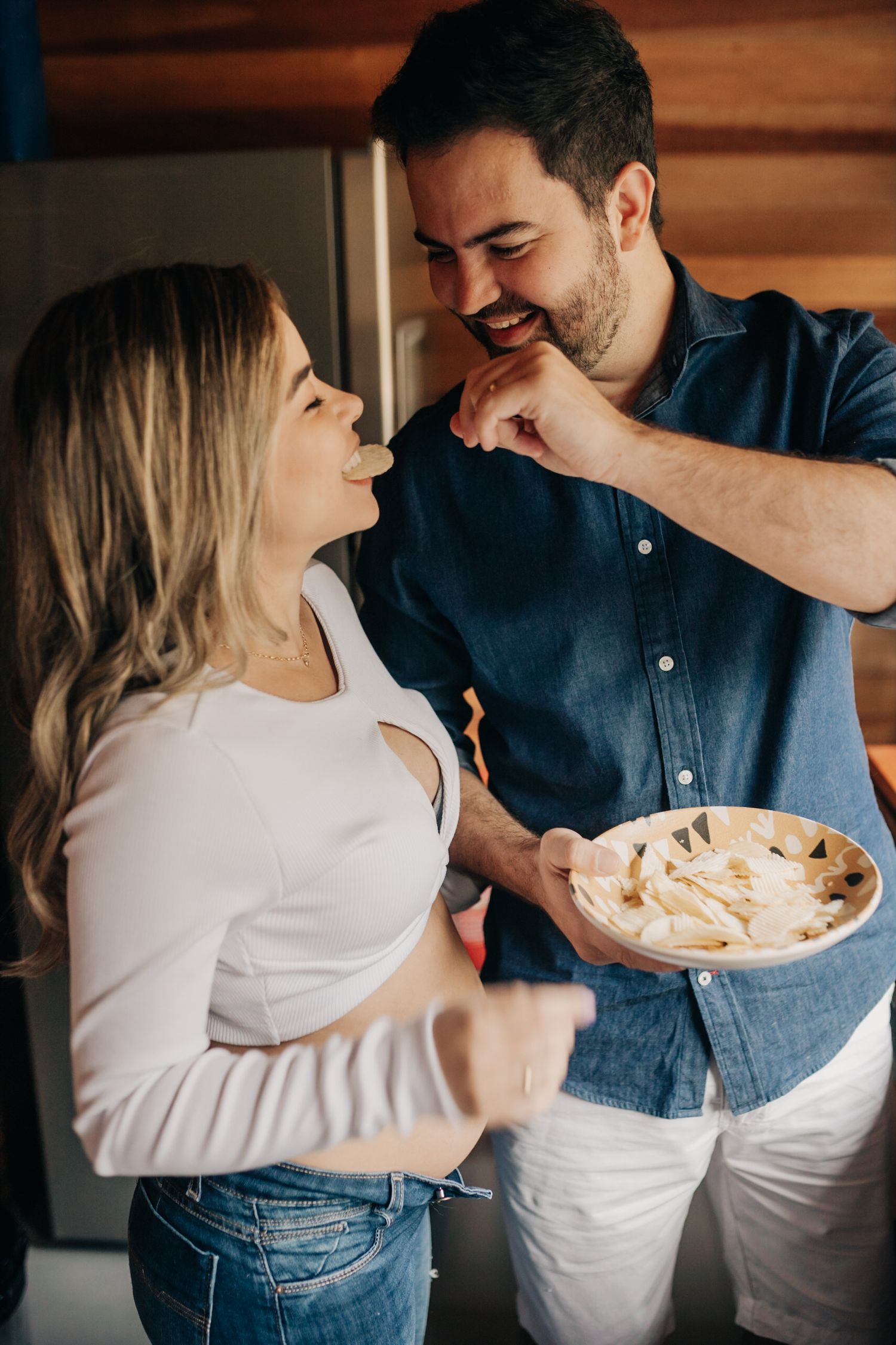 Couple enjoying playful moments while sharing a bowl of food in a rustic setting.