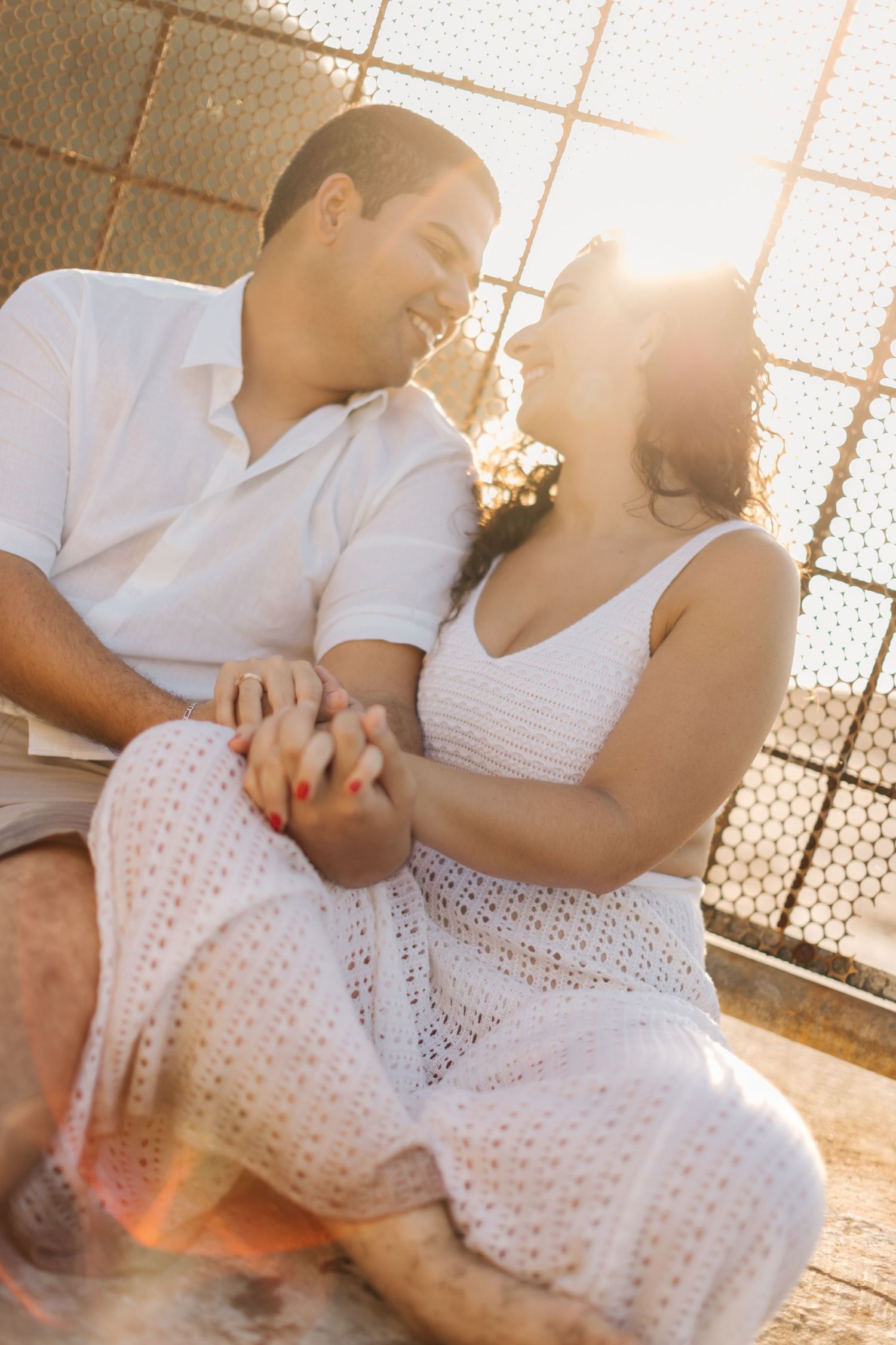 Couple holding hands and sharing loving glances in sunlit setting.