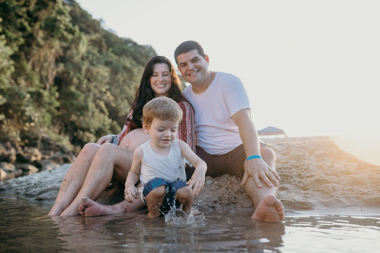 Family having fun at the beach during golden hour, walking in shallow water together.