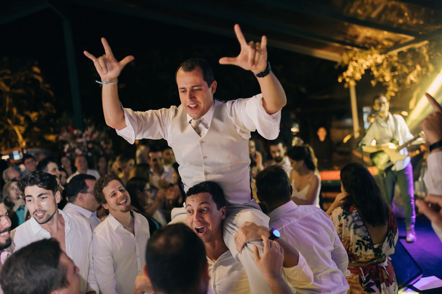 Wedding guest raises hands in celebration among the dancing crowd at a reception.