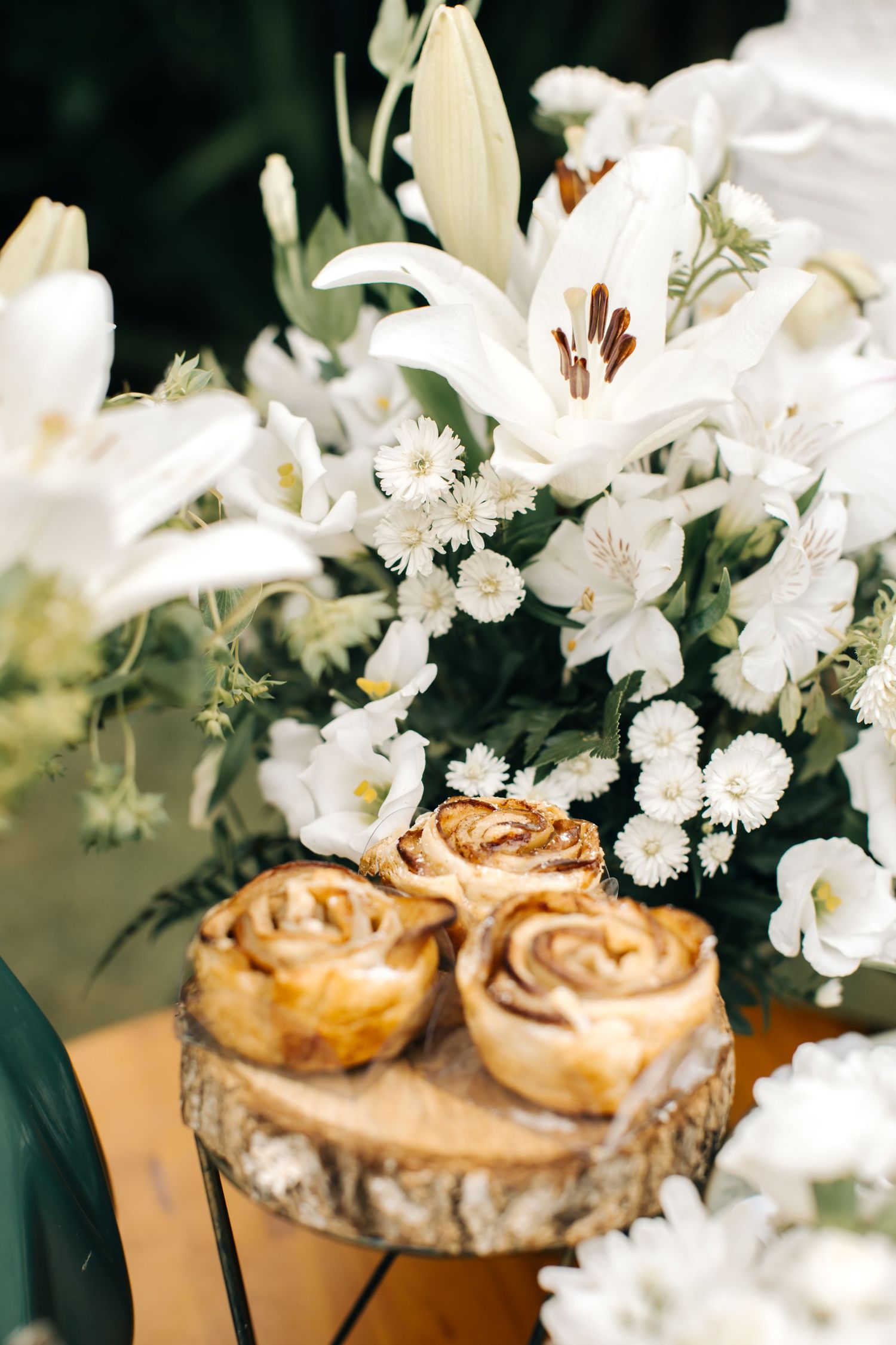 White floral centerpiece with pastries displayed on rustic wooden slice.