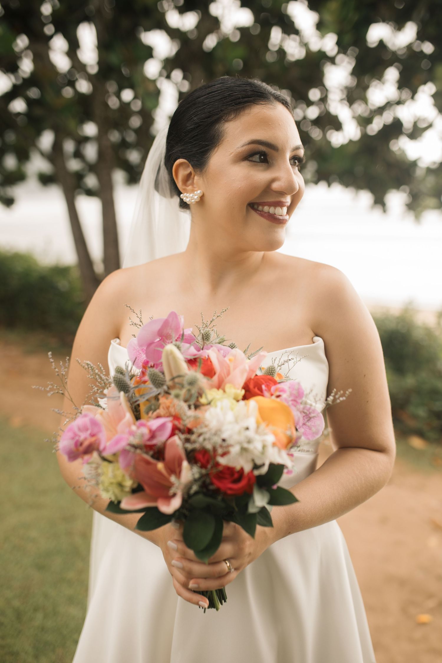 A bride holds a vibrant pink and orange bouquet during an outdoor wedding photoshoot.