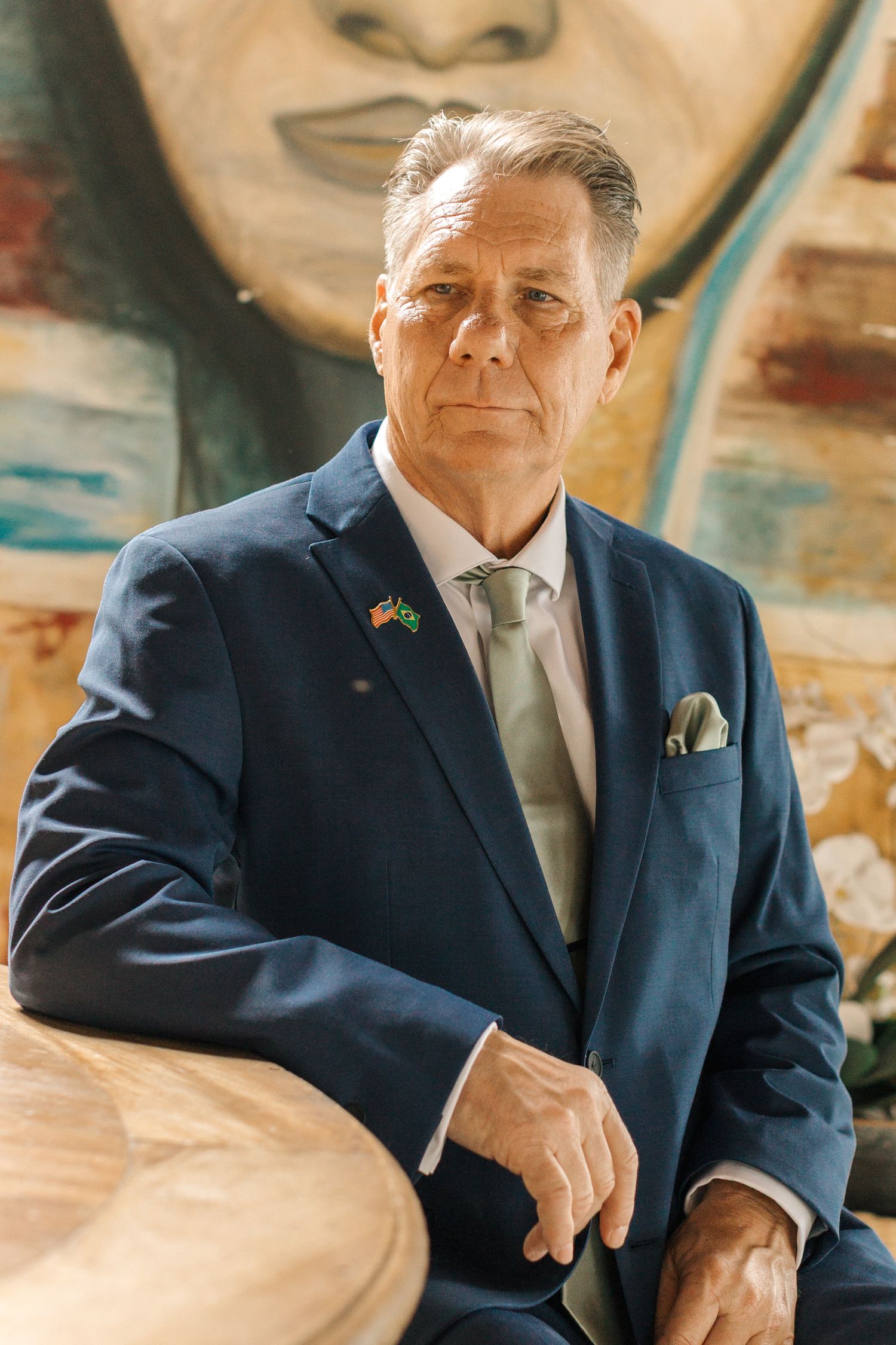 Person in a dark blue suit sitting casually indoors with warm lighting and decor.