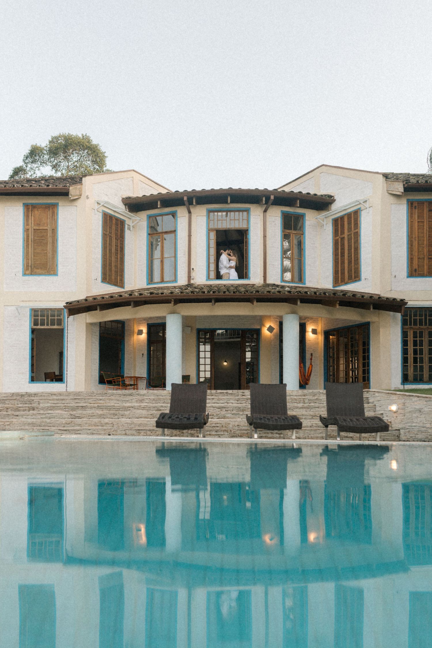 Mediterranean-style villa with white walls and stone columns reflects in a tranquil swimming pool at dusk.