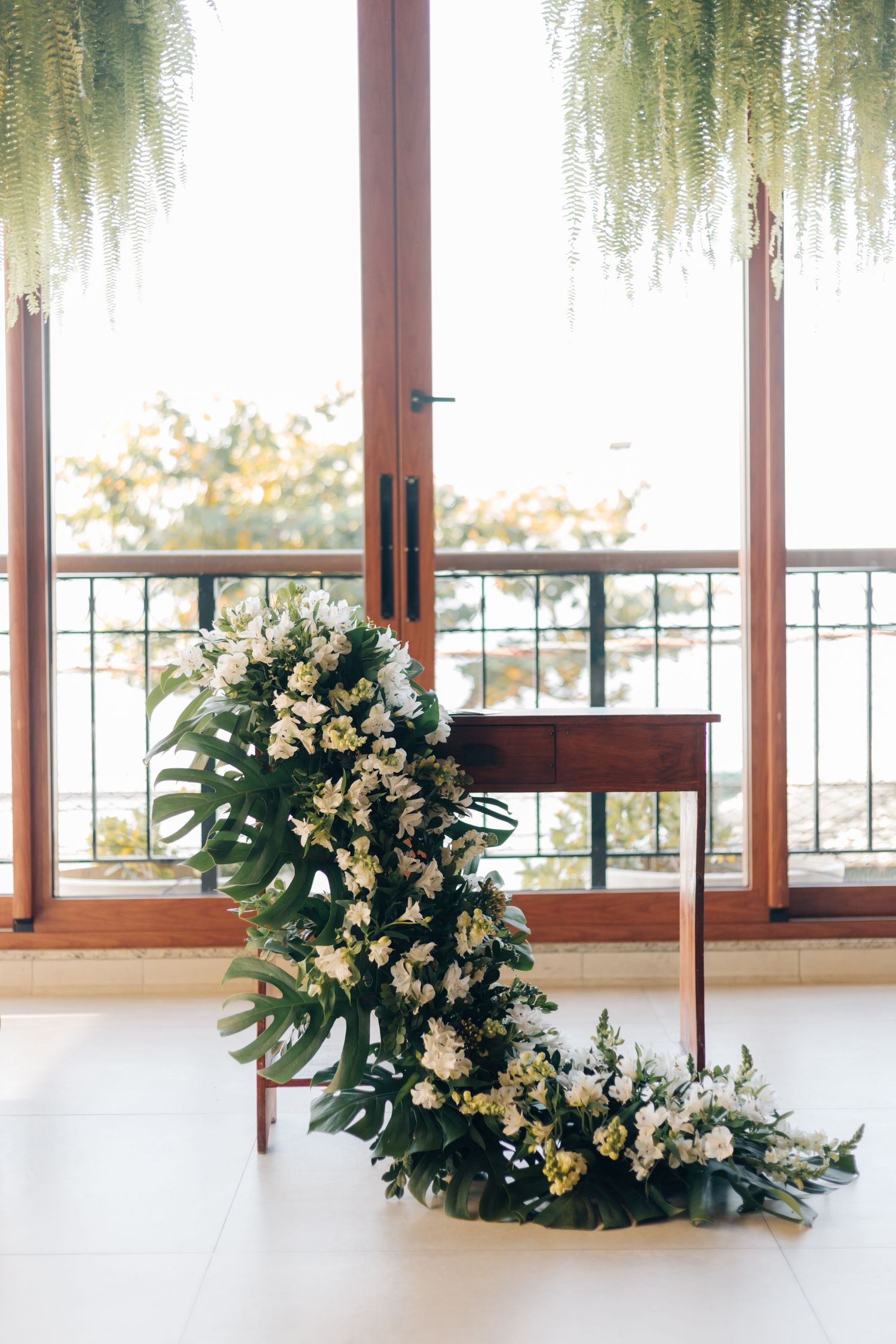 Elegant floral arrangement with white flowers and greenery decorates a bright windowed venue.