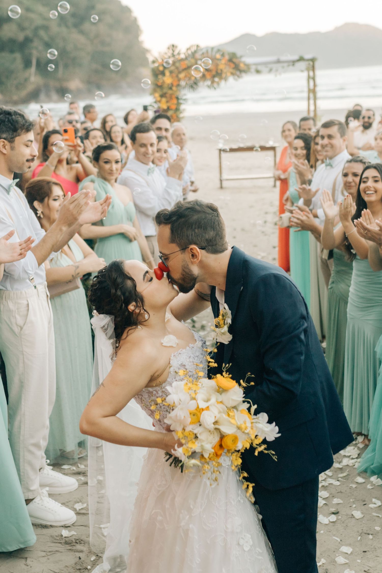 A beautiful beach wedding ceremony with guests in mint green dresses and floating bubbles in the air.