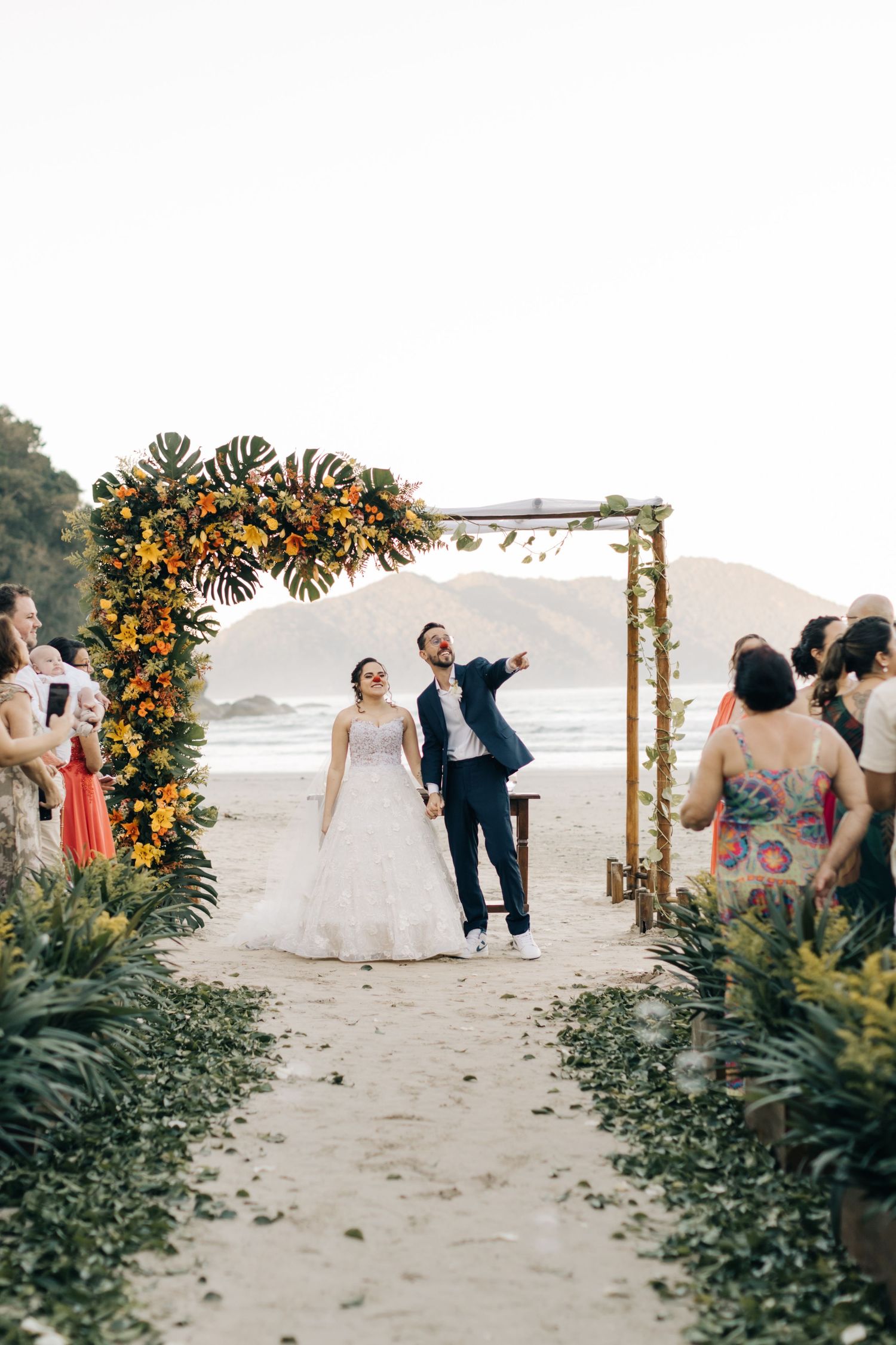 A beach wedding ceremony setup with floral arch and guests on sandy shores.