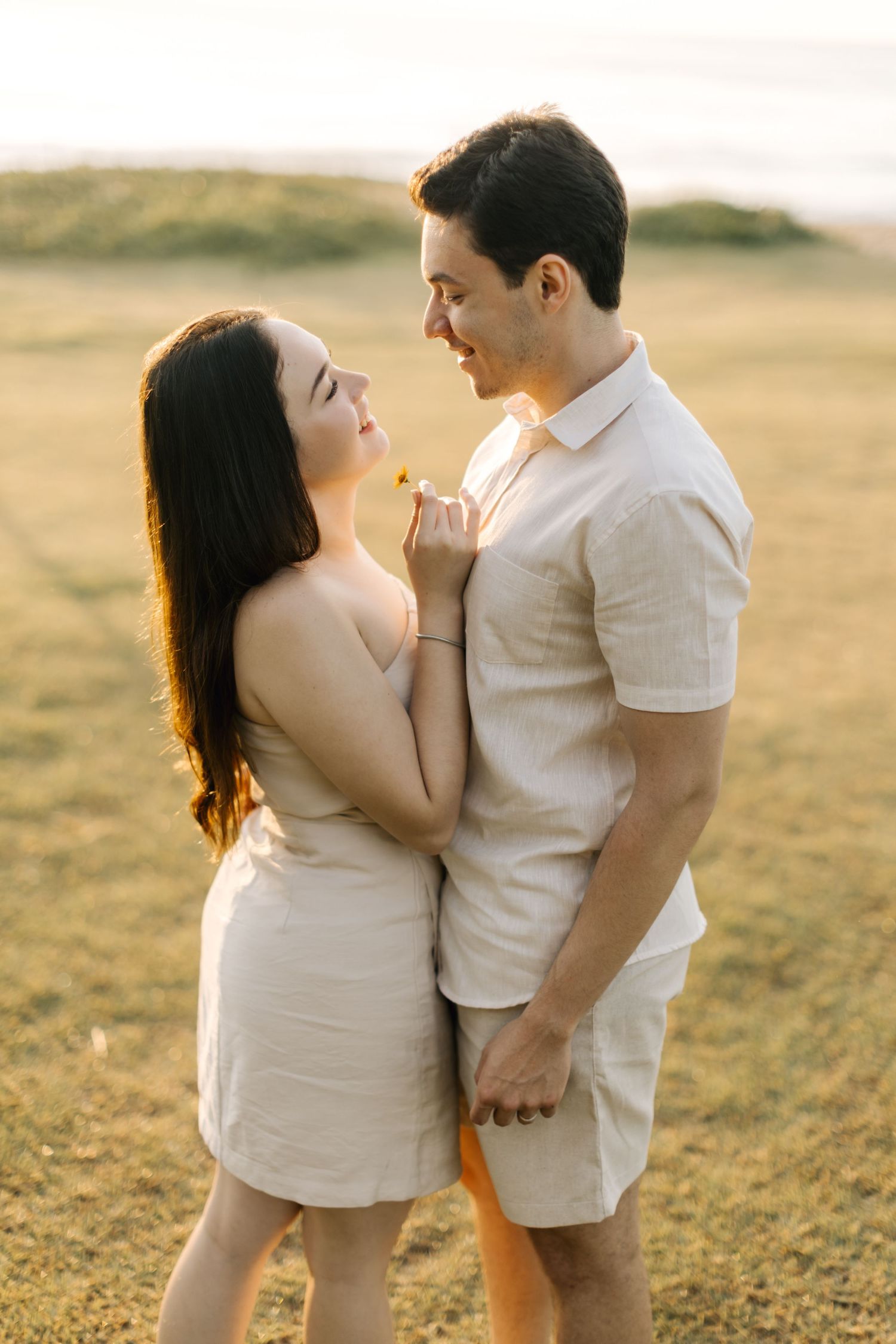 Tender moment between couple wearing coordinated beige outfits during golden hour photoshoot.