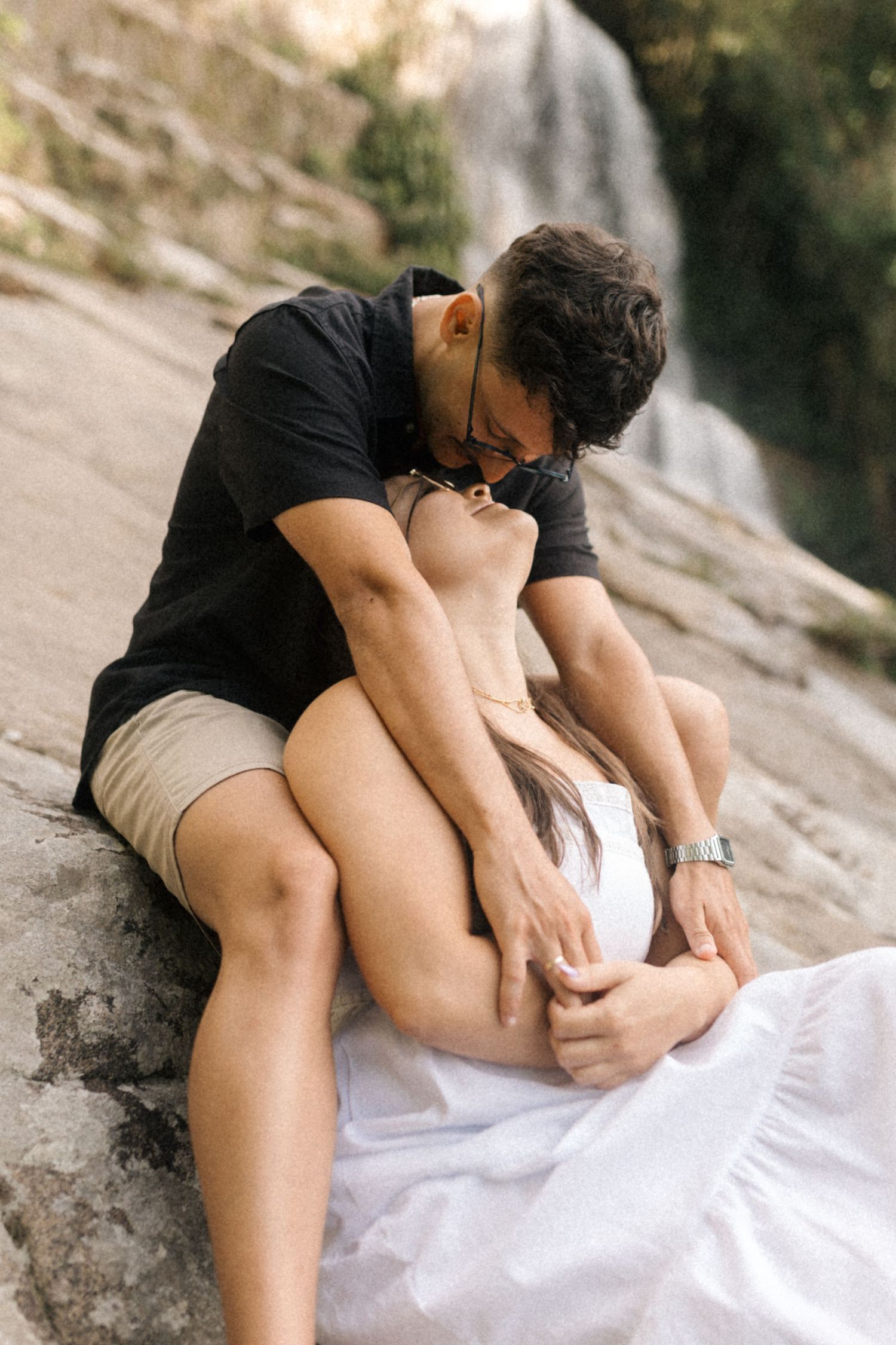 Intimate photoshoot sequence showing a couple embracing on rocky terrain by a waterfall.