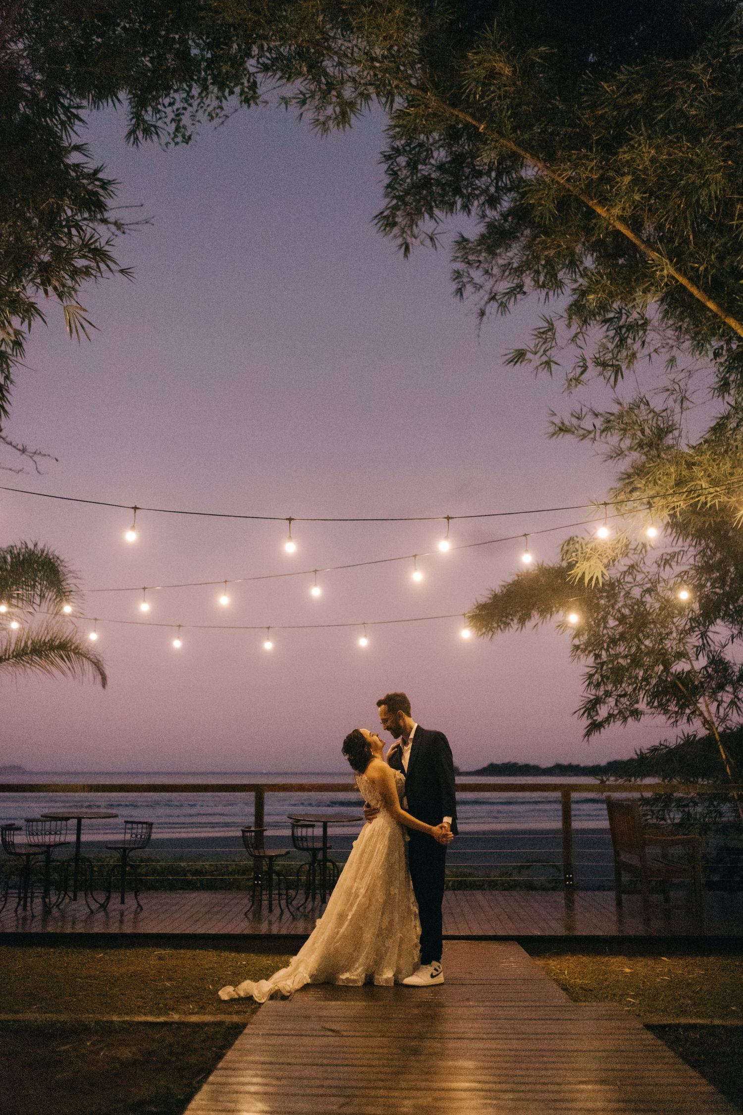 A couple dancing under string lights at their beach wedding reception.