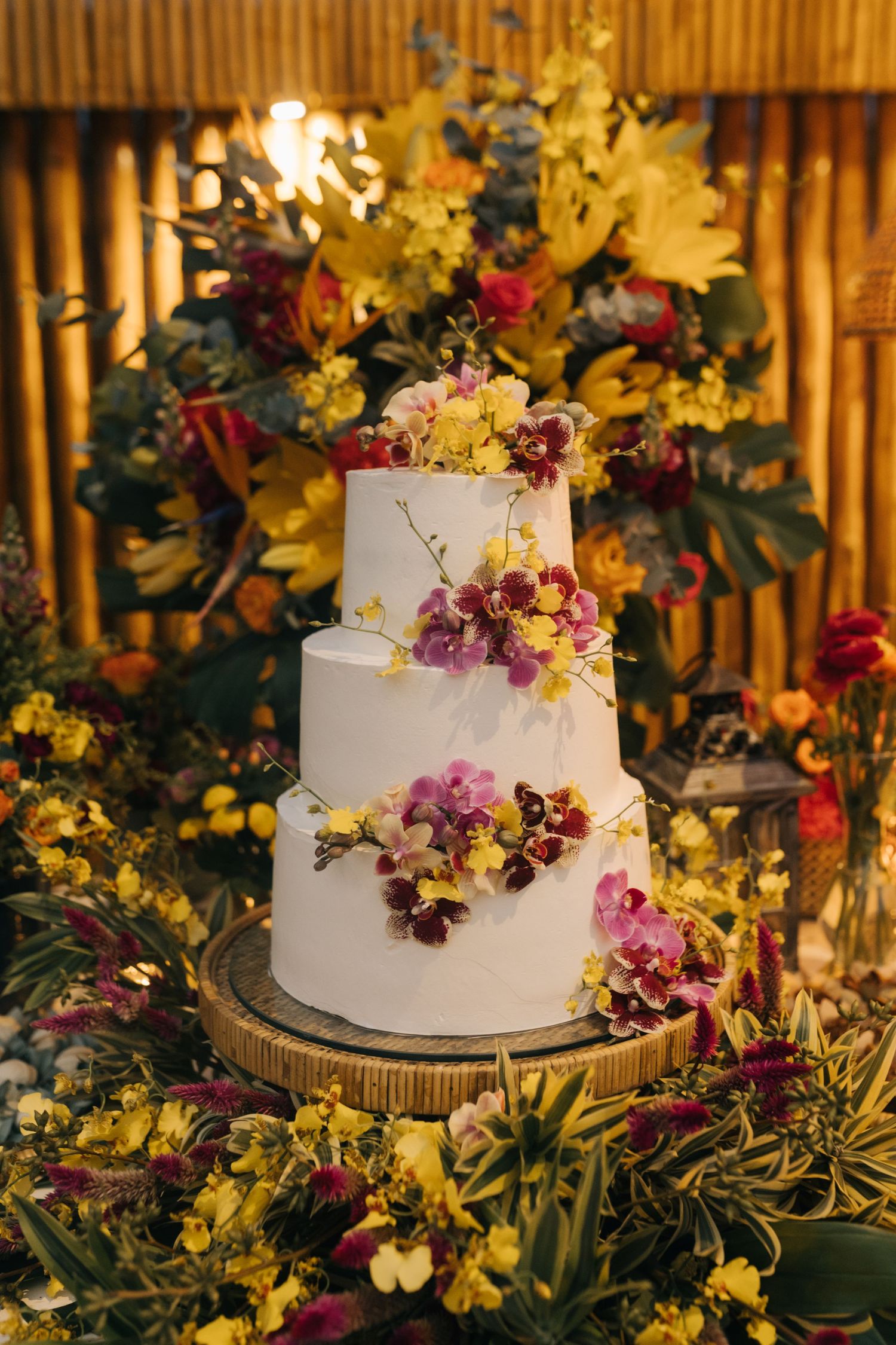 Elegant white tiered wedding cake adorned with cascading purple and pink flowers on a wooden stand.