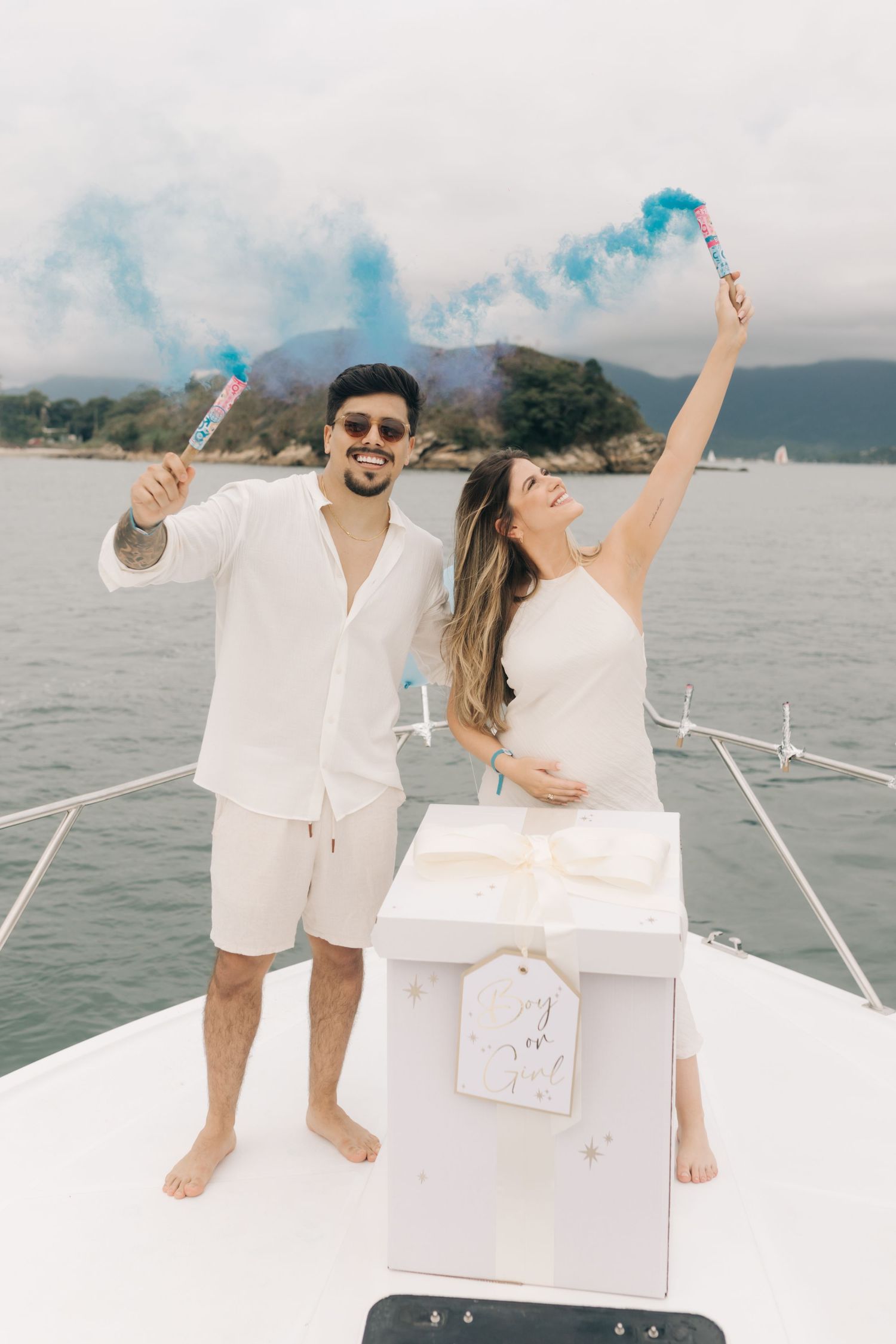 Couple celebrating with blue smoke flares on a boat deck overlooking coastal waters.