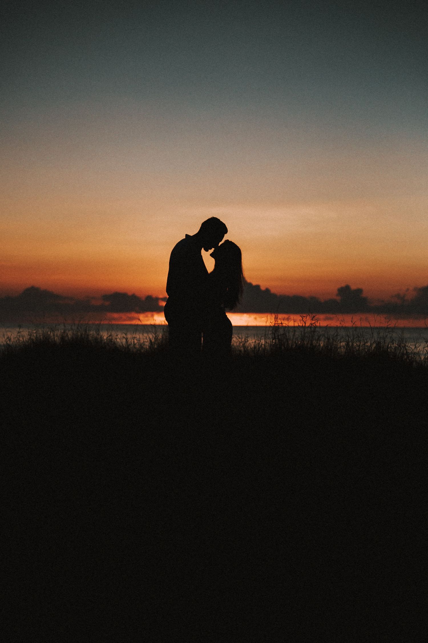 Silhouettes of a couple against a vibrant orange and purple sunset sky.