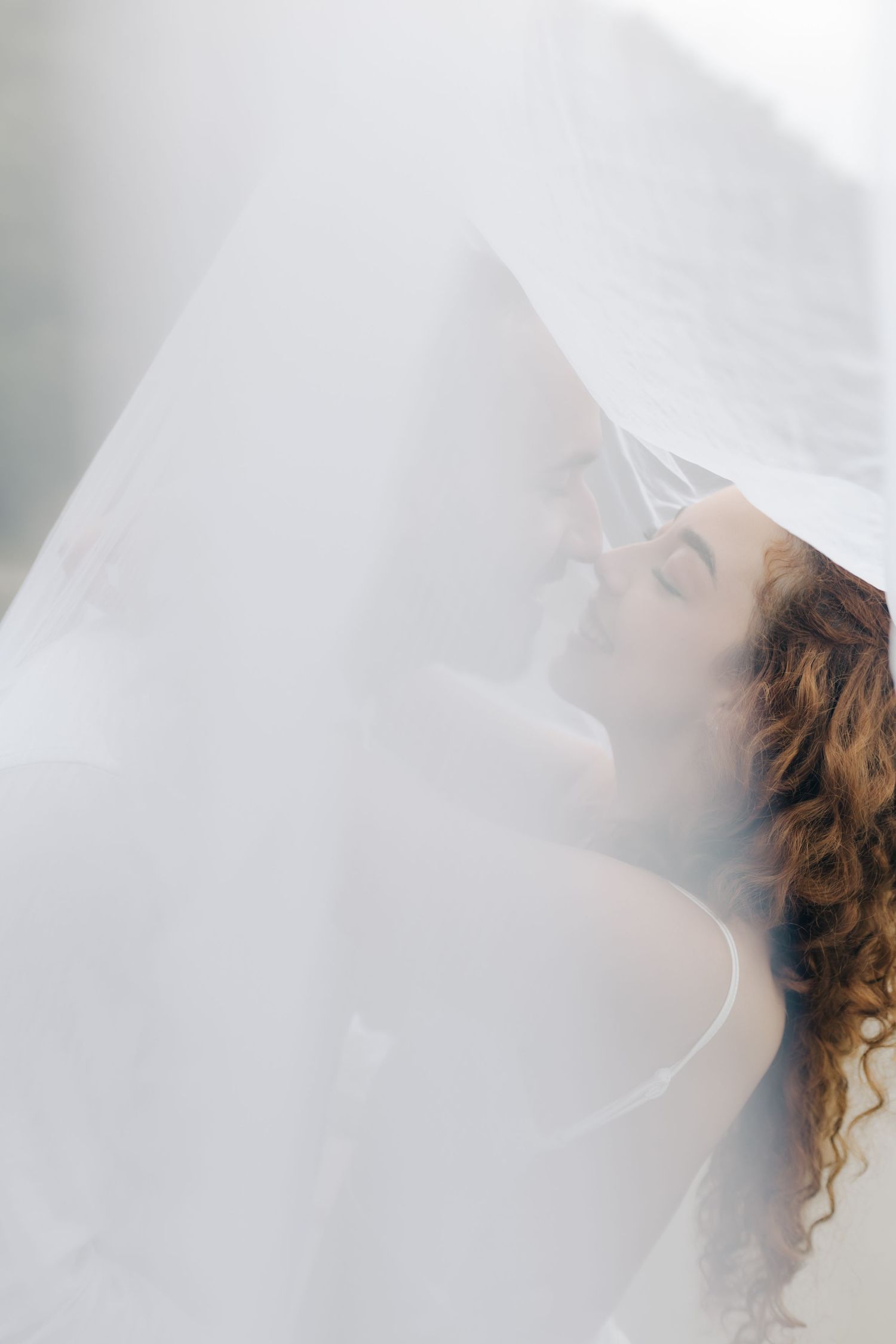 Ethereal bridal portrait through flowing white veil creating dreamy atmosphere.