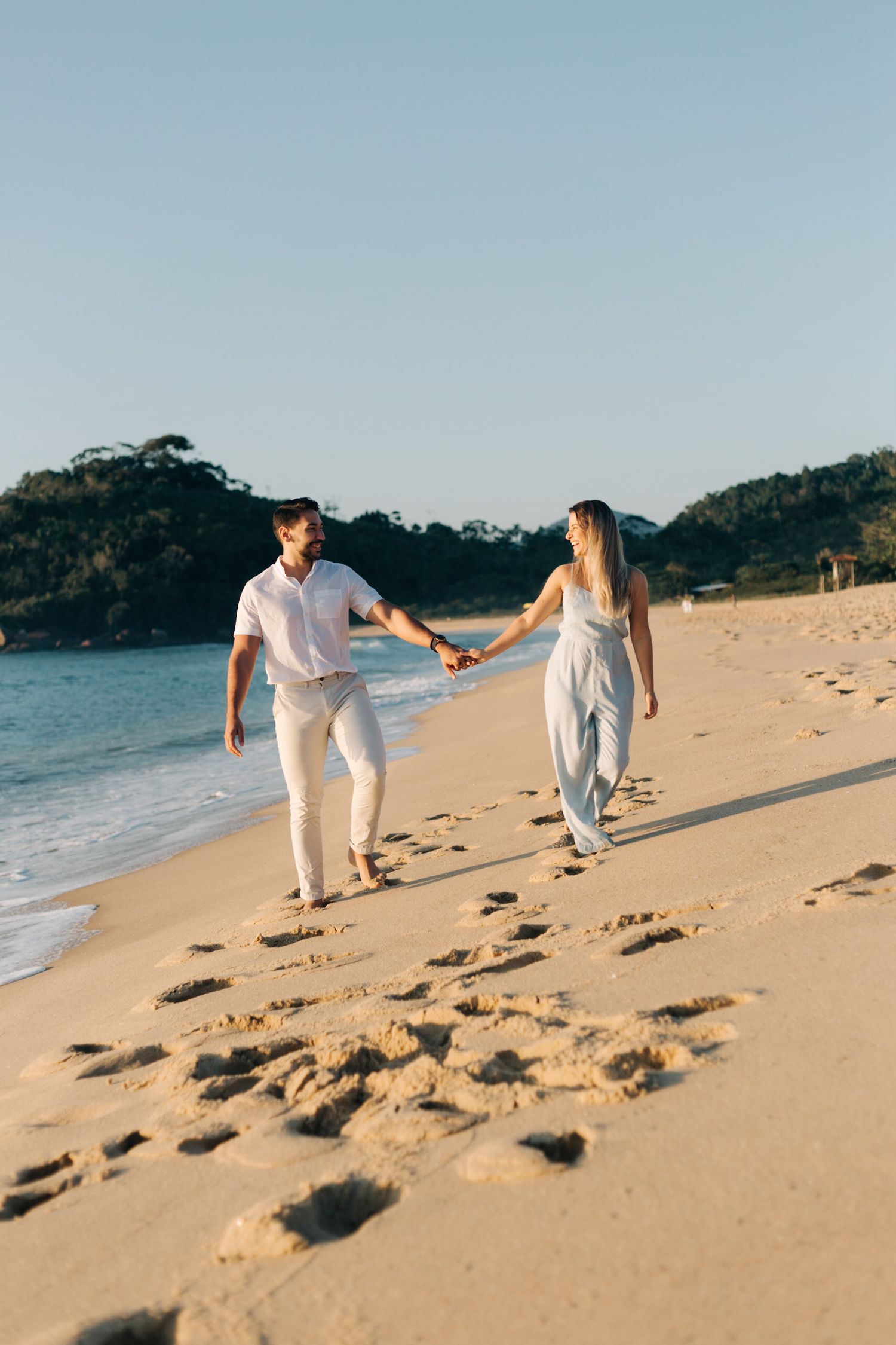 Romantic beach walk captured from behind as couple in white clothing stroll along the shoreline.