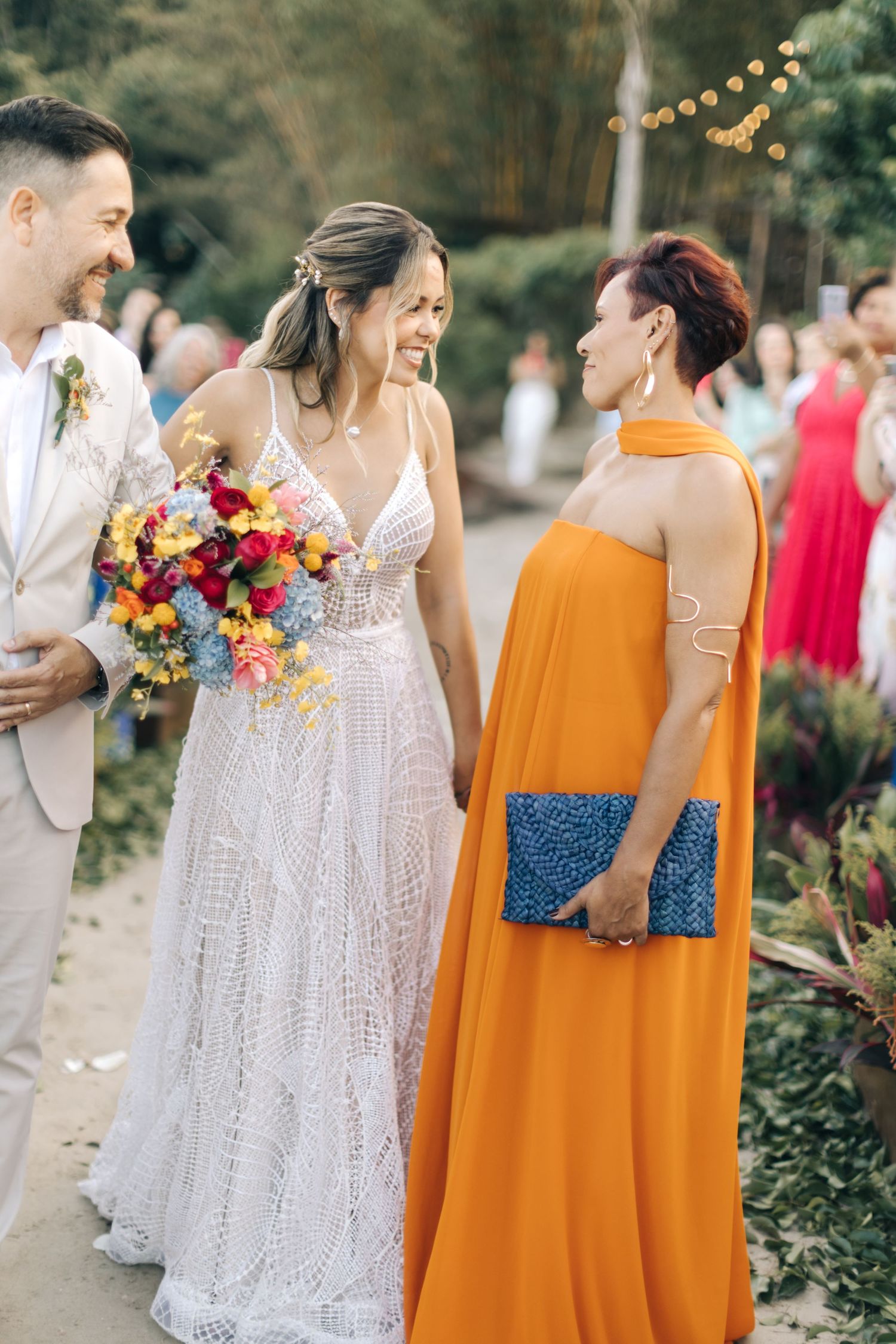 Candid wedding moment captured on garden path with white lace gown and bright orange dress.