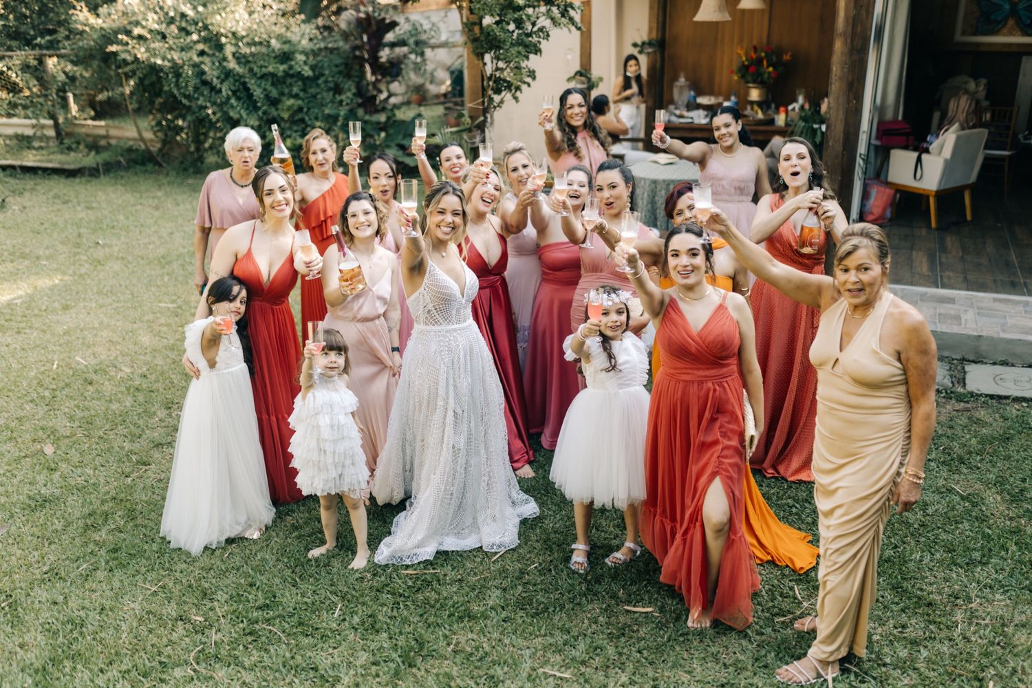Wedding party group photo featuring attendants in coral and pink dresses with flower girls in white tutus.